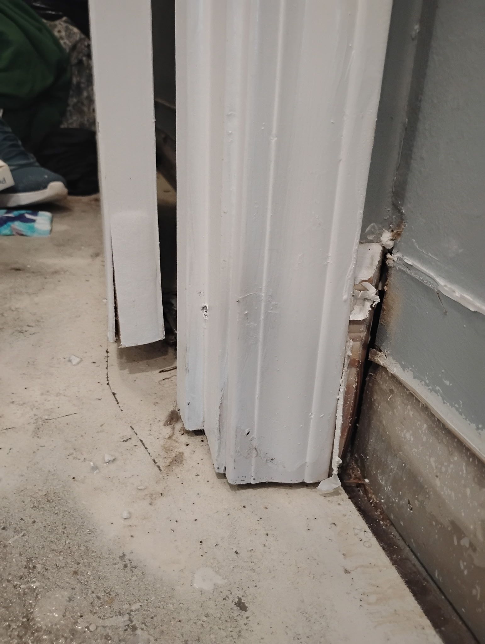 White door frame on concrete floor next to a dark-stained wall.