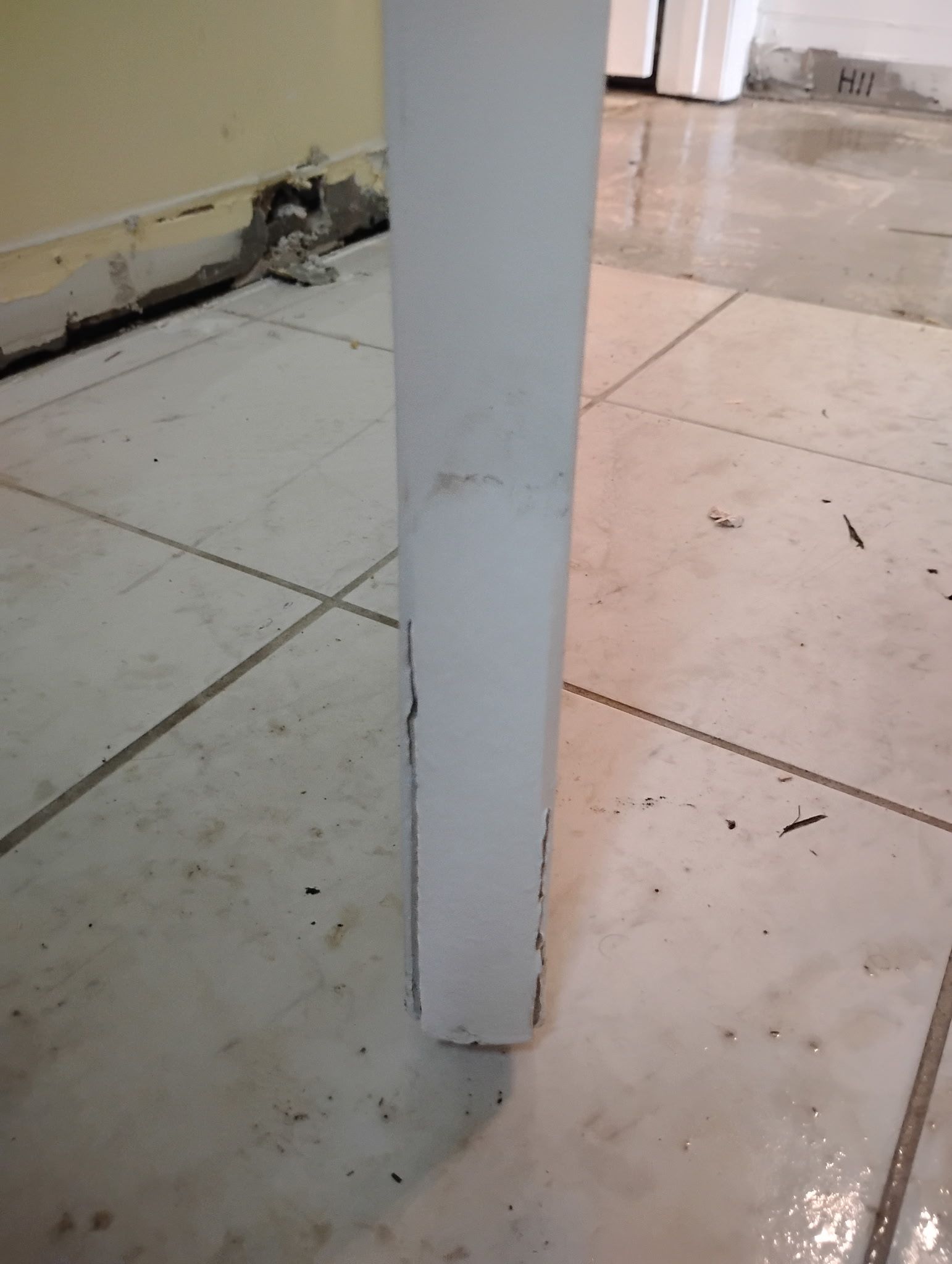 White pillar on tile floor, base near wall with concrete debris.