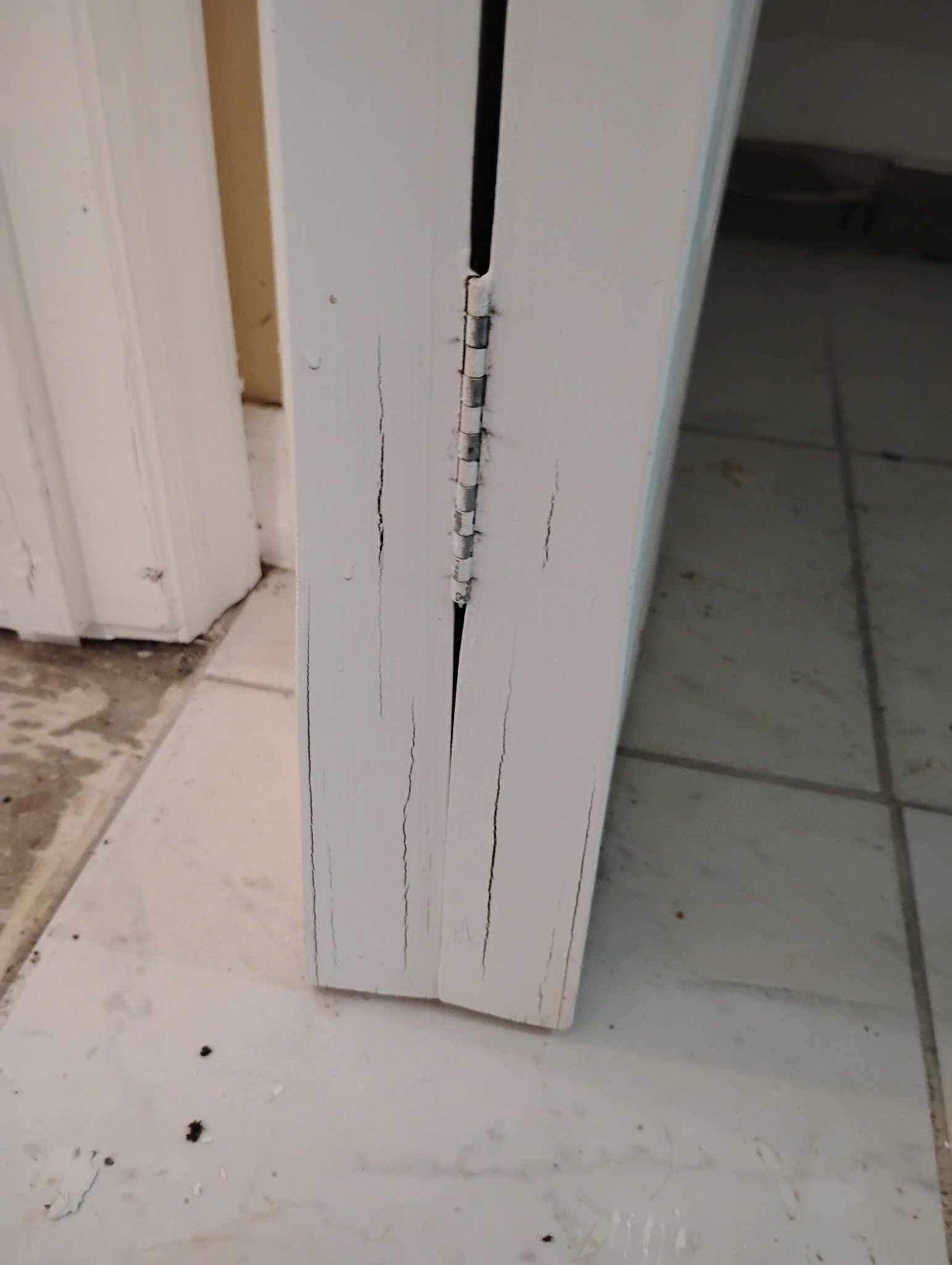 White door frame with vertical cracks and wear, on a tiled floor.
