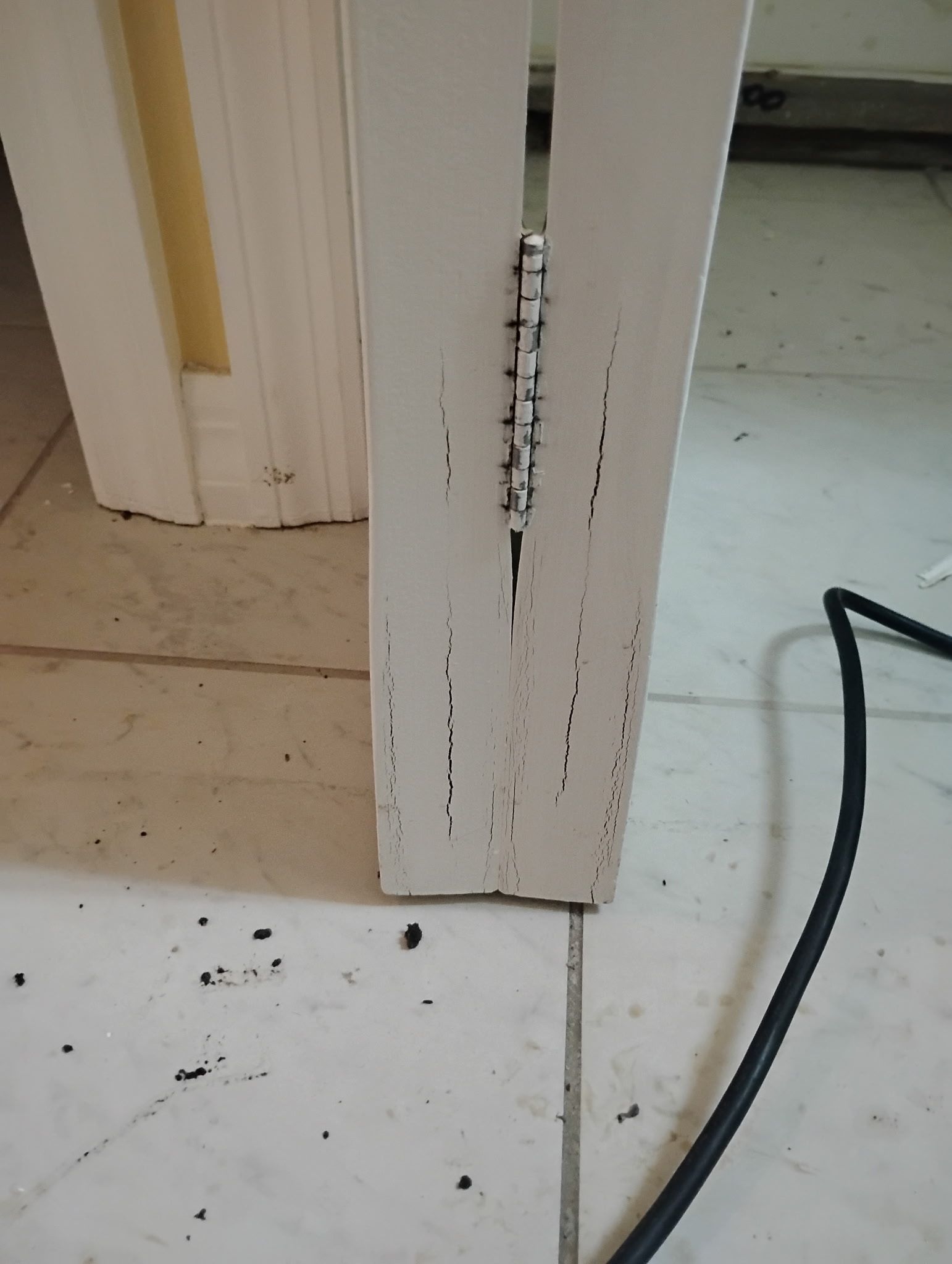White door frame with a hinge and screw holes. Small debris on the floor.