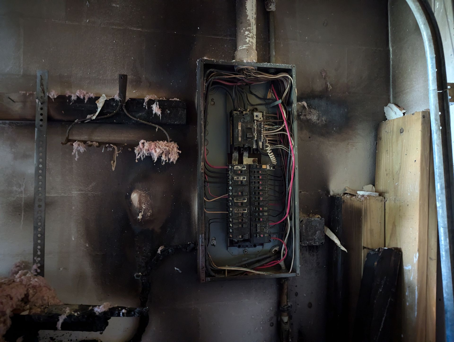 An electrical box that has been damaged by a fire is hanging on a wall.