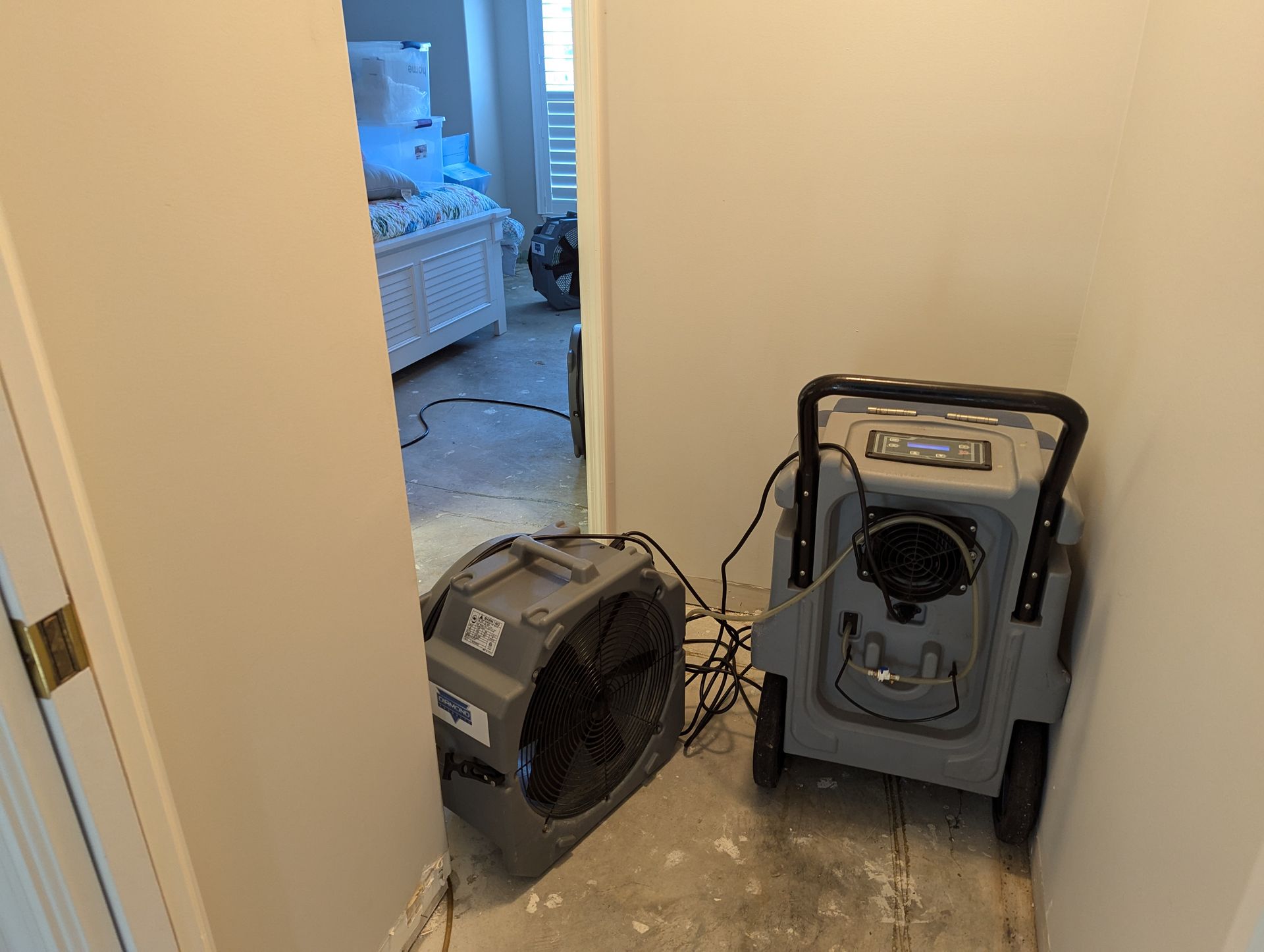 Two fans are sitting on the floor in a room next to a door.