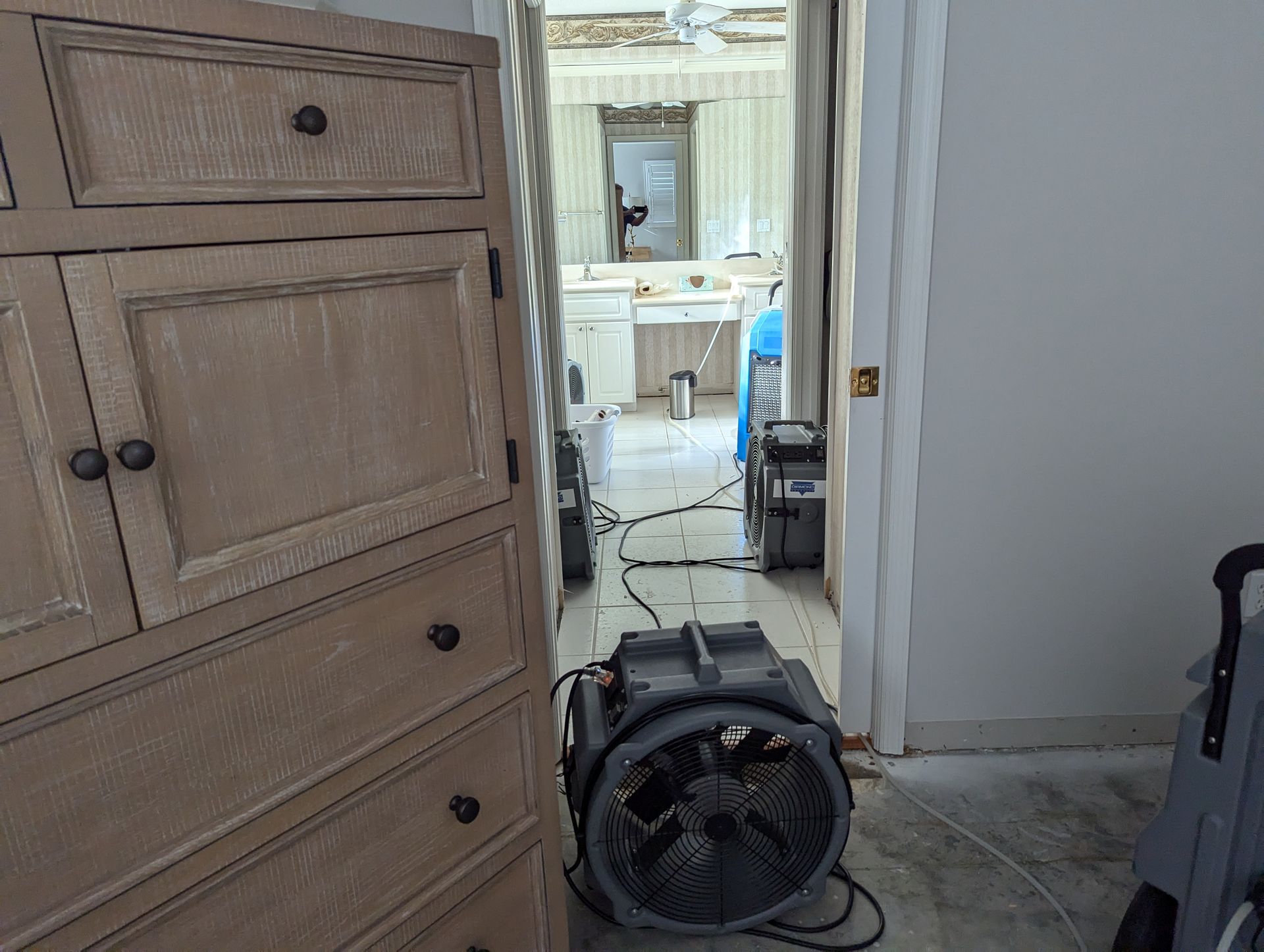 A fan is sitting in a room next to a dresser.