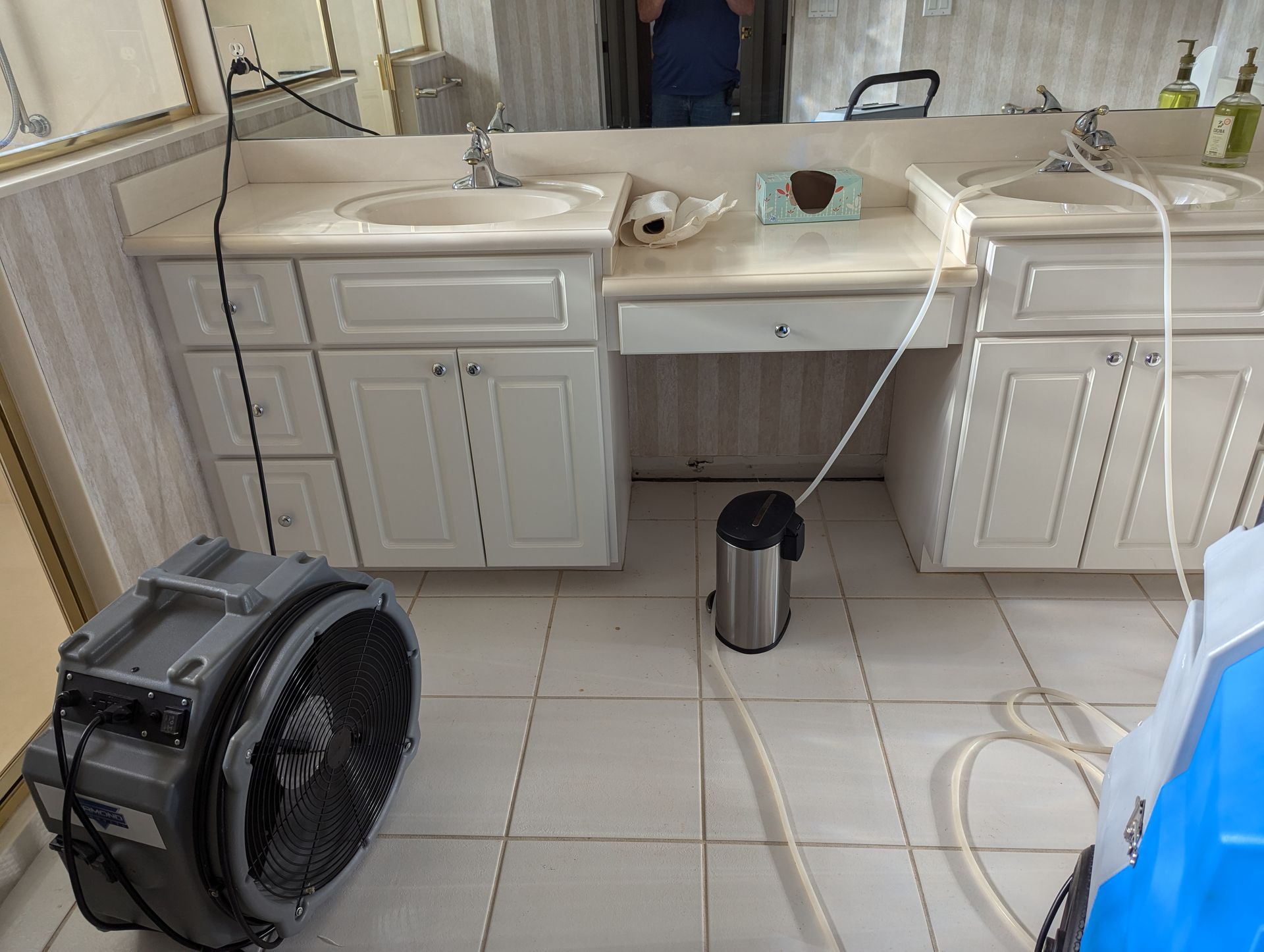 A bathroom with two sinks and a fan on the floor.