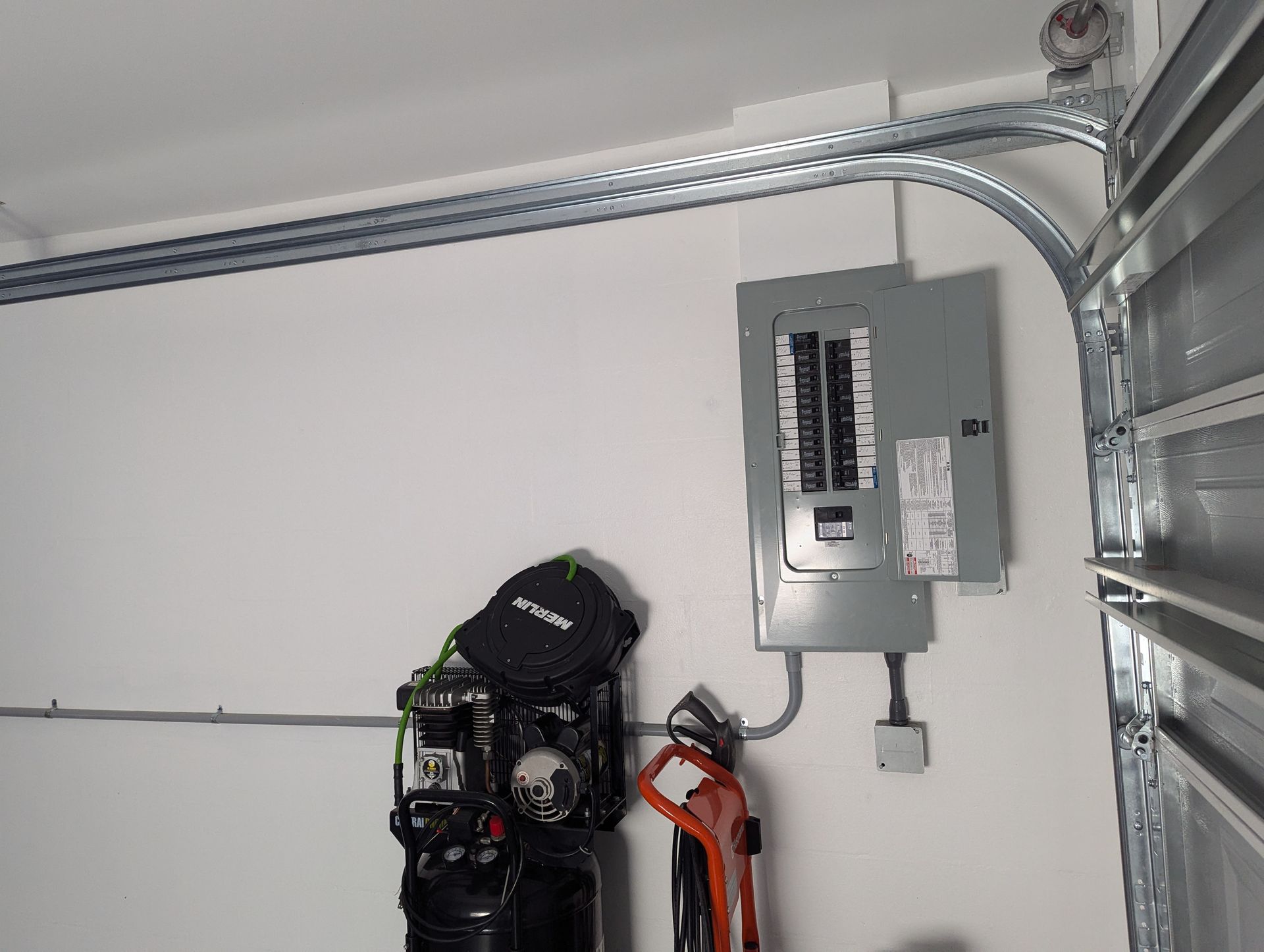 An electrical box is hanging on a wall next to a garage door.