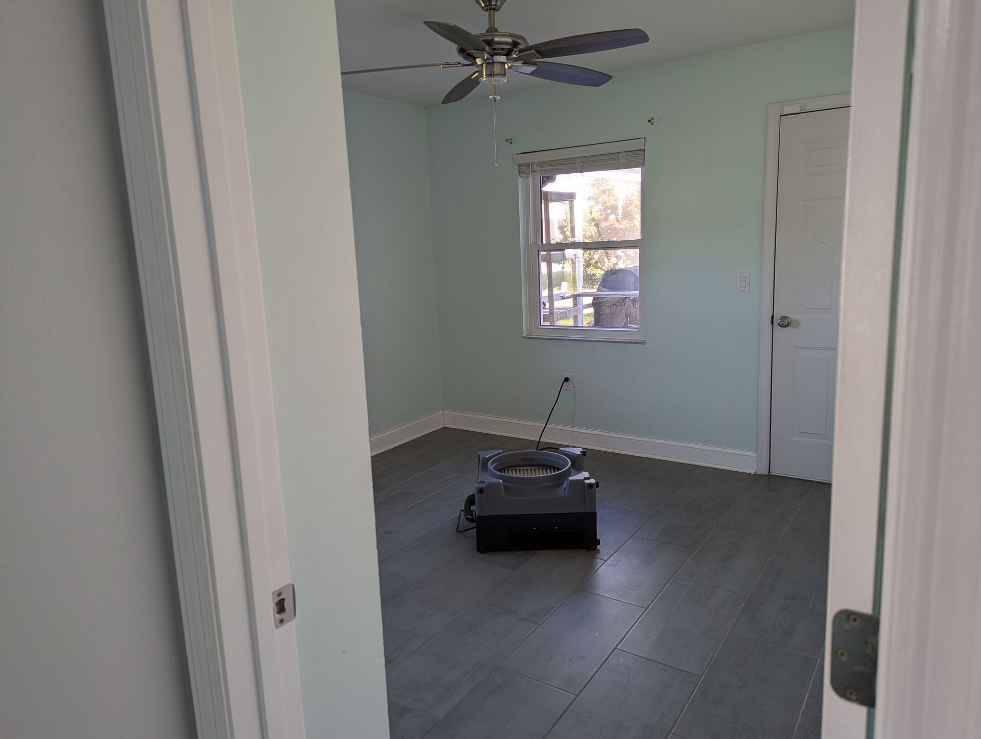 An empty room with a ceiling fan and a window.