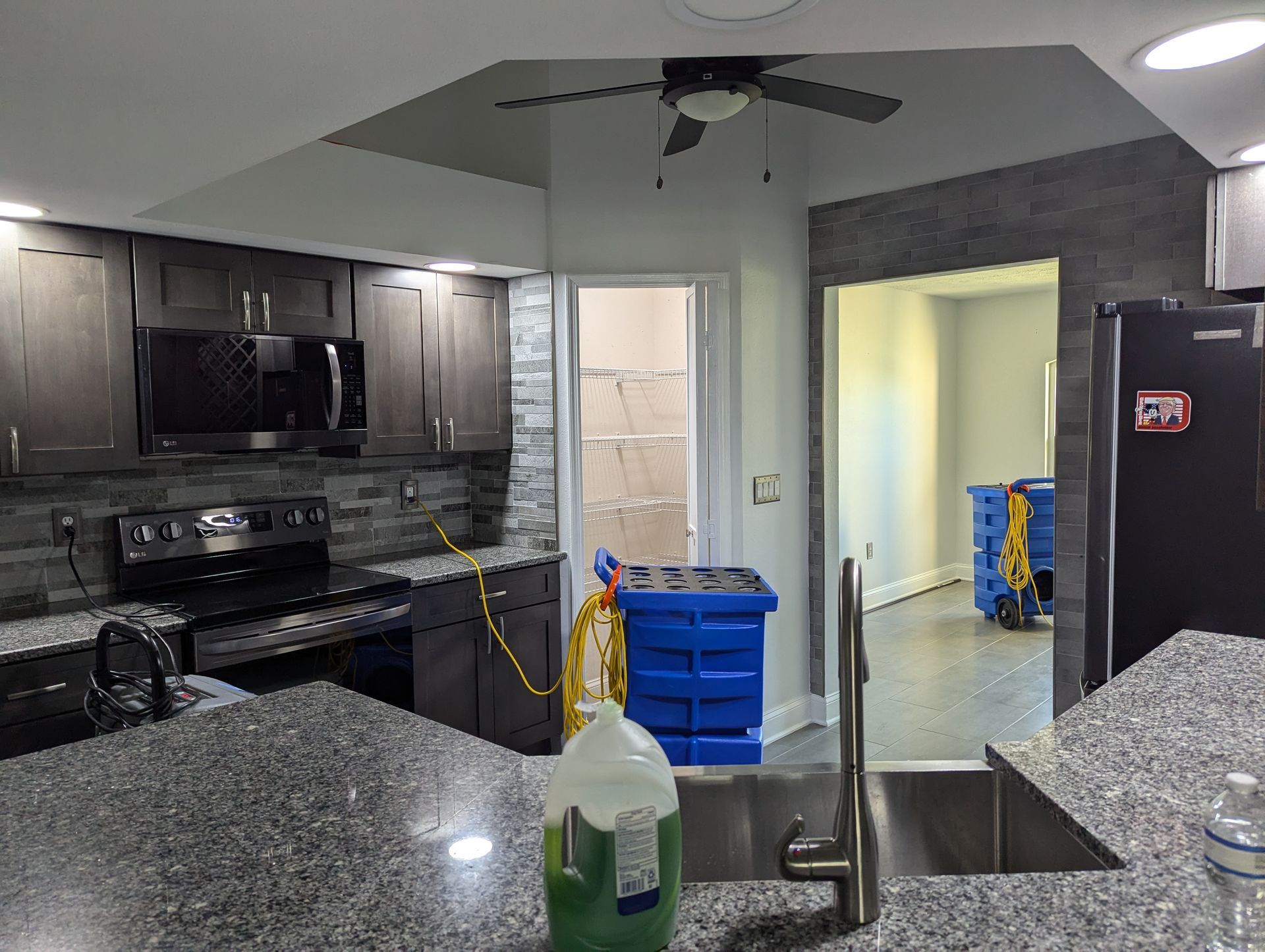 A kitchen with a sink , stove , microwave and a ceiling fan.