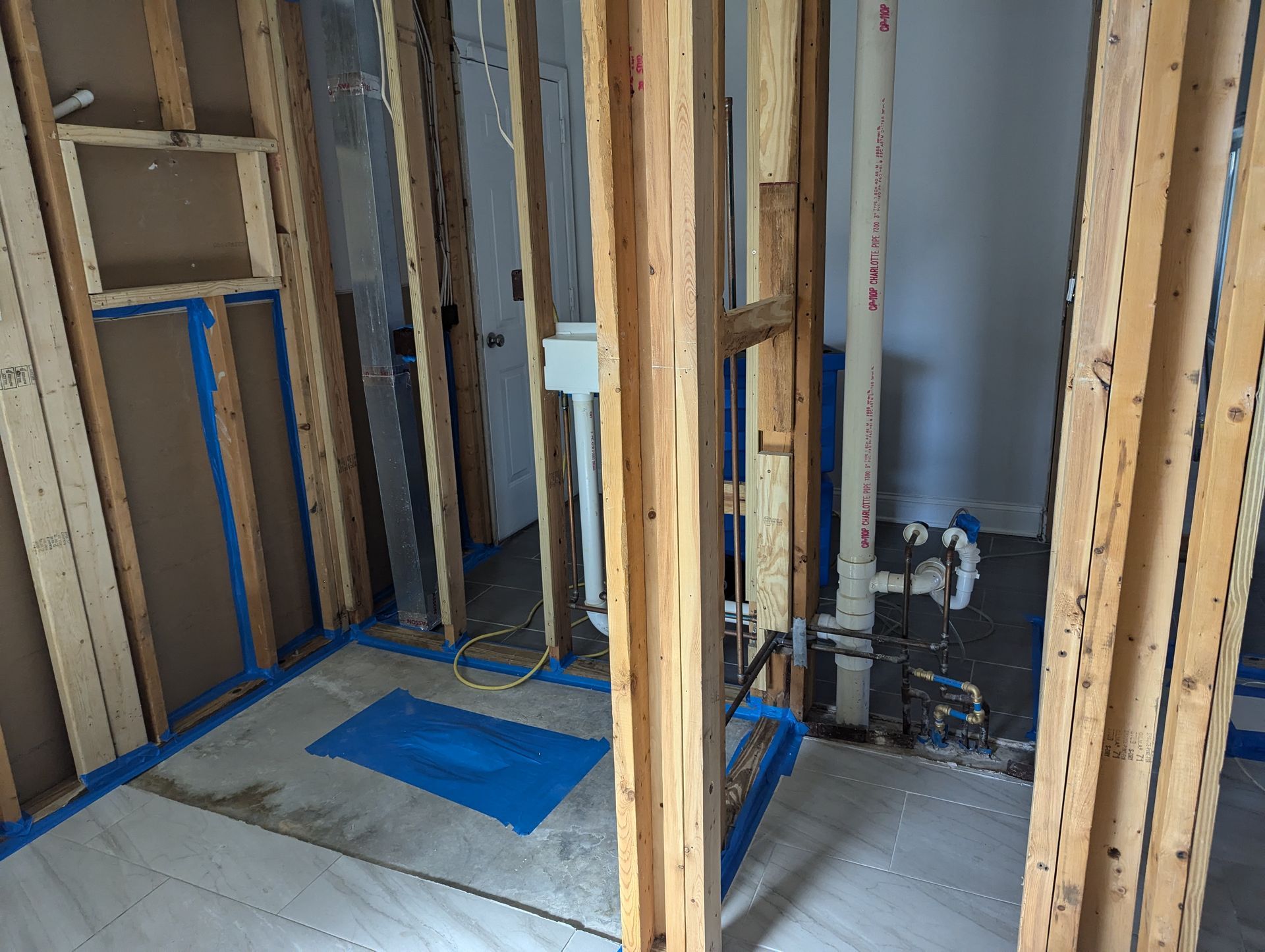 A bathroom under construction with blue tape on the floor.