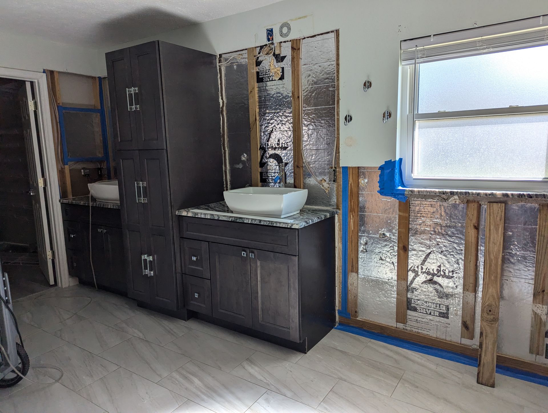 A bathroom under construction with a sink , cabinets , and a window.