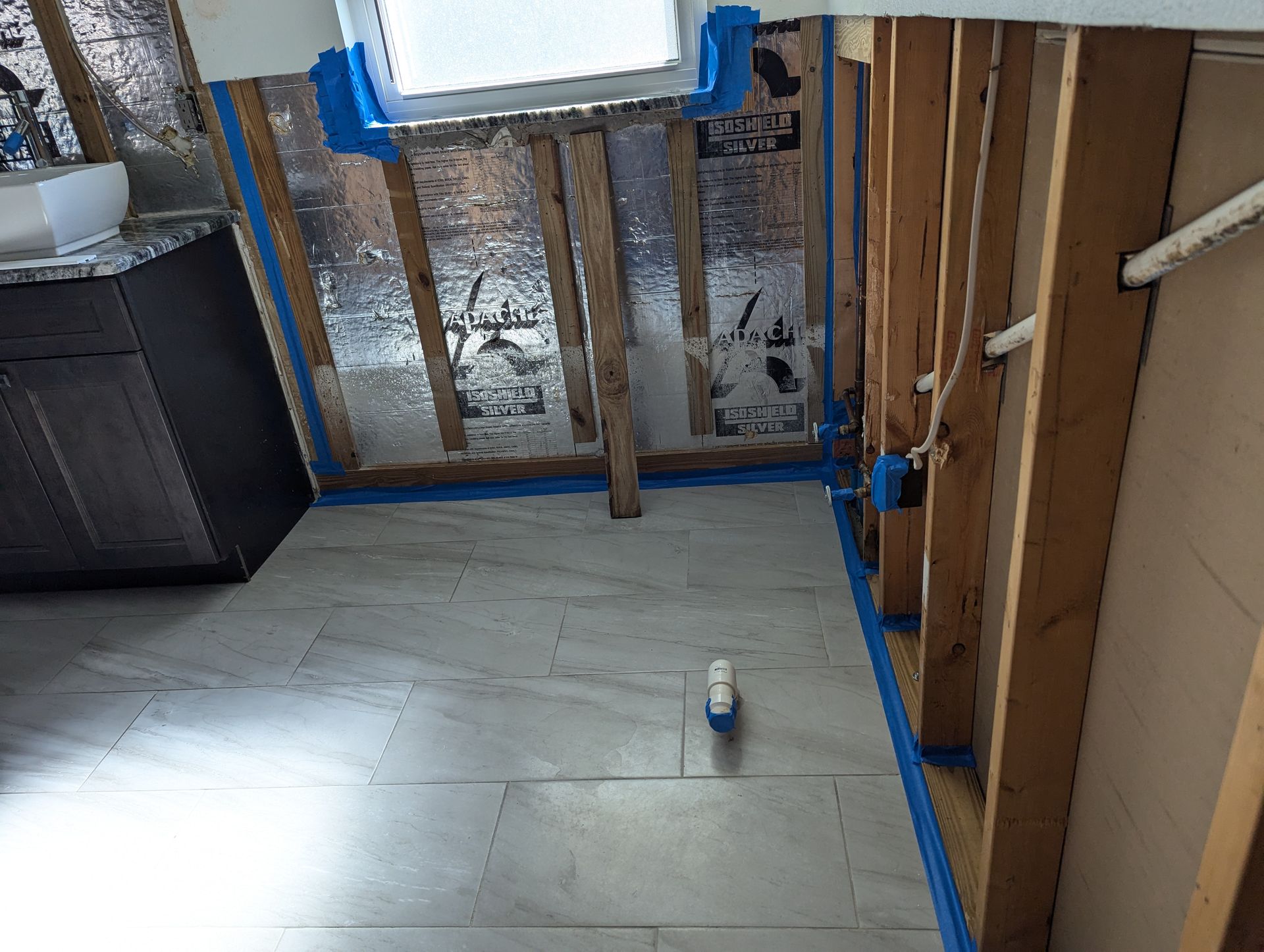 A bathroom under construction with blue tape on the floor and walls.
