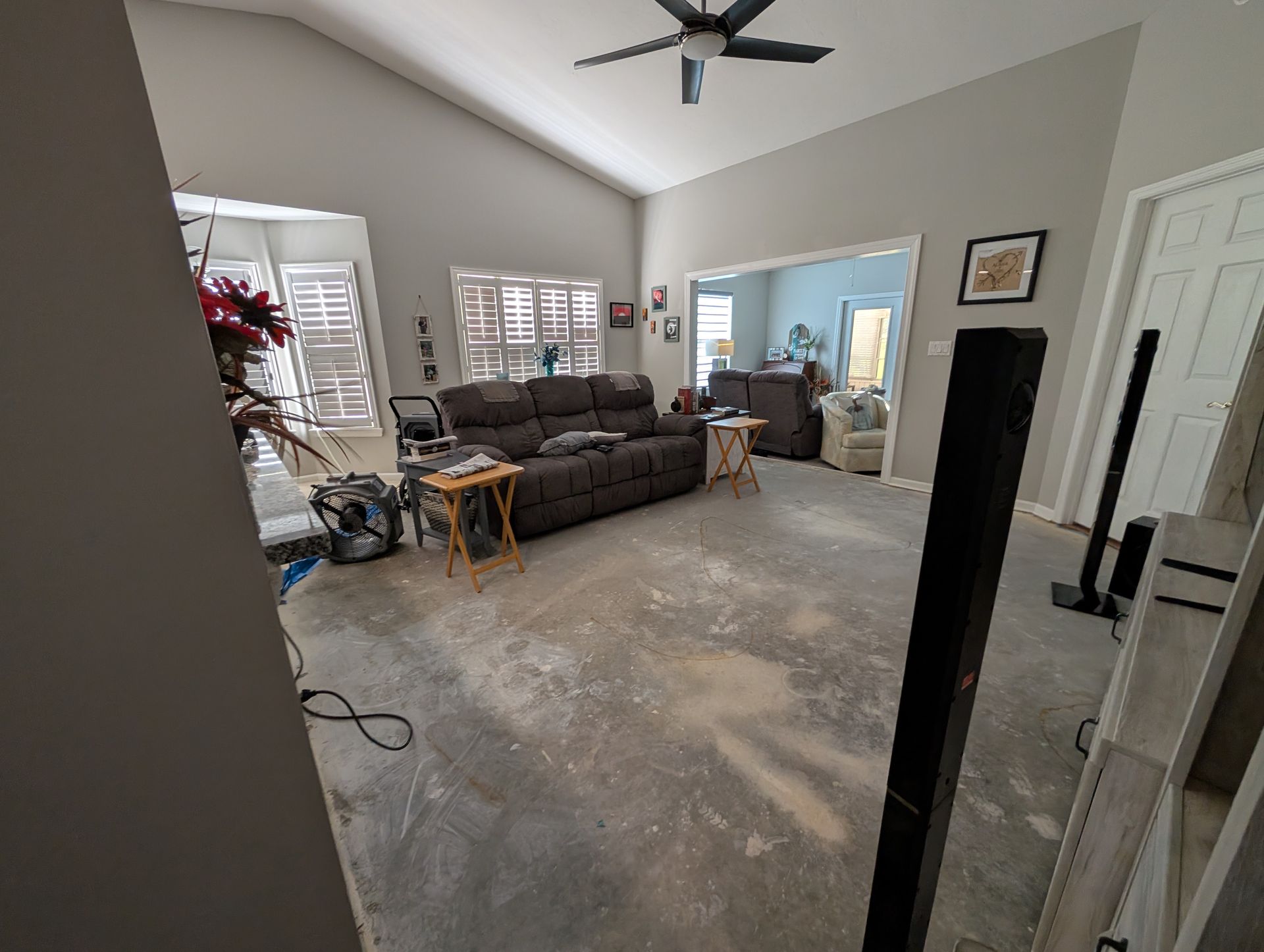 Living room with a sofa, side tables, and a doorway. The floor appears to be under construction.
