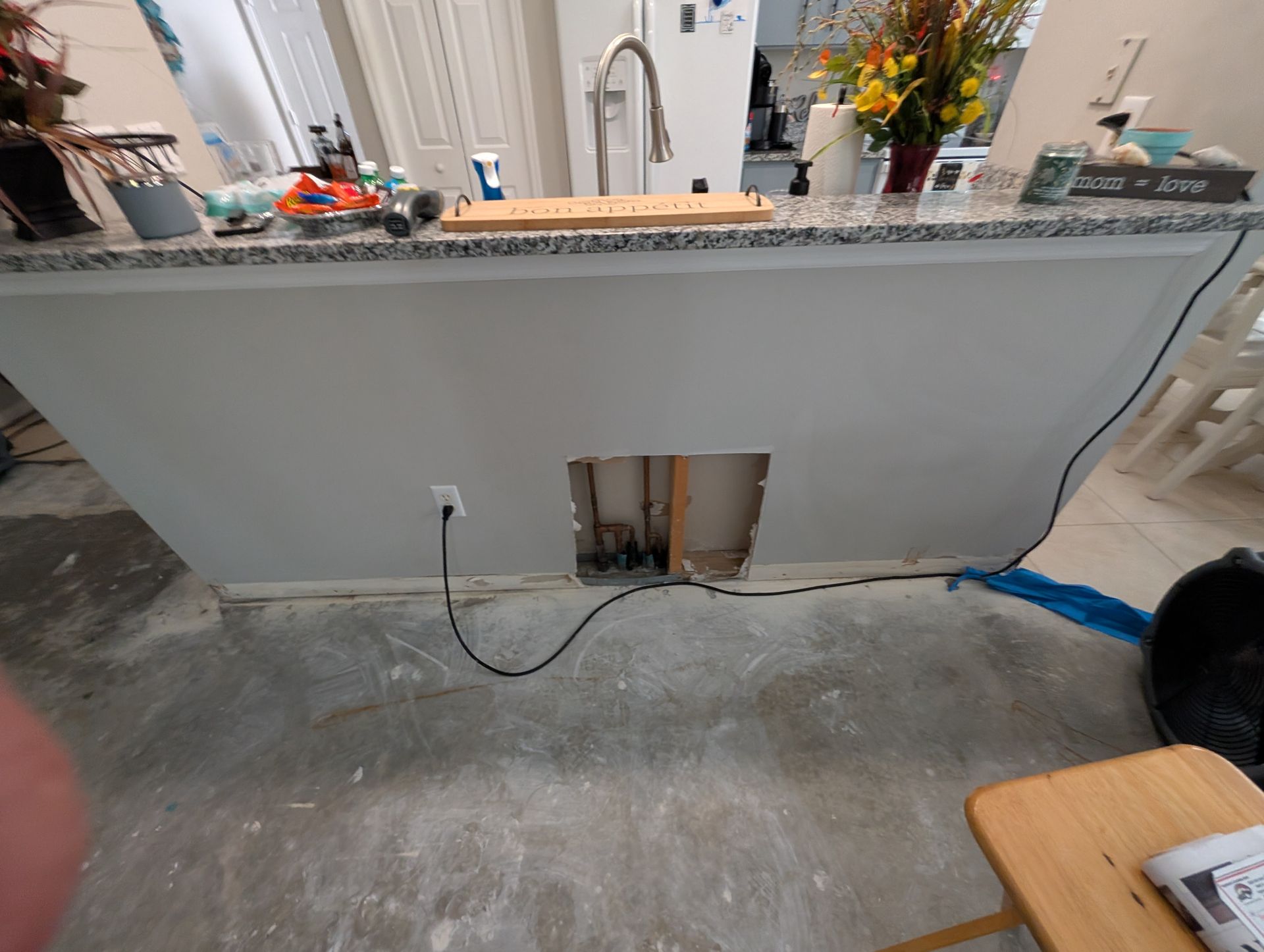 Kitchen island with a hole in the wall, electrical outlet, and exposed wiring; construction setting.