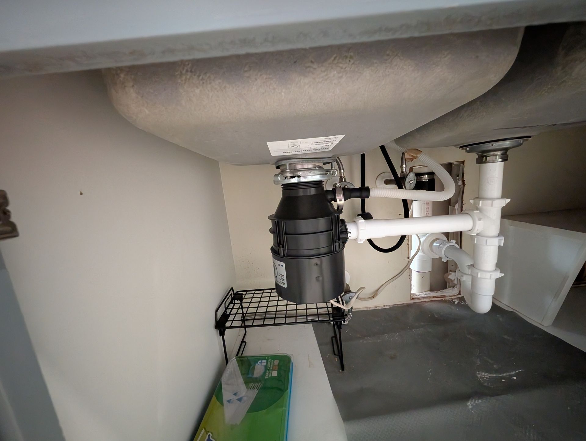 Under-sink plumbing: garbage disposal, pipes, and drains beneath a kitchen sink.