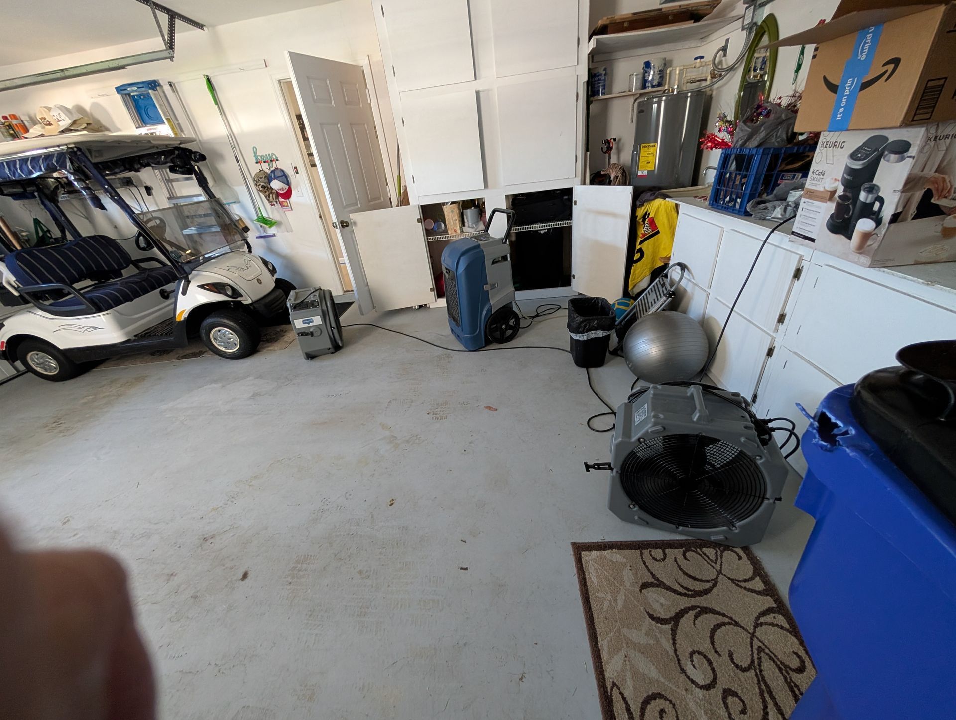 Garage with golf carts, fans, storage, and various equipment on a concrete floor.