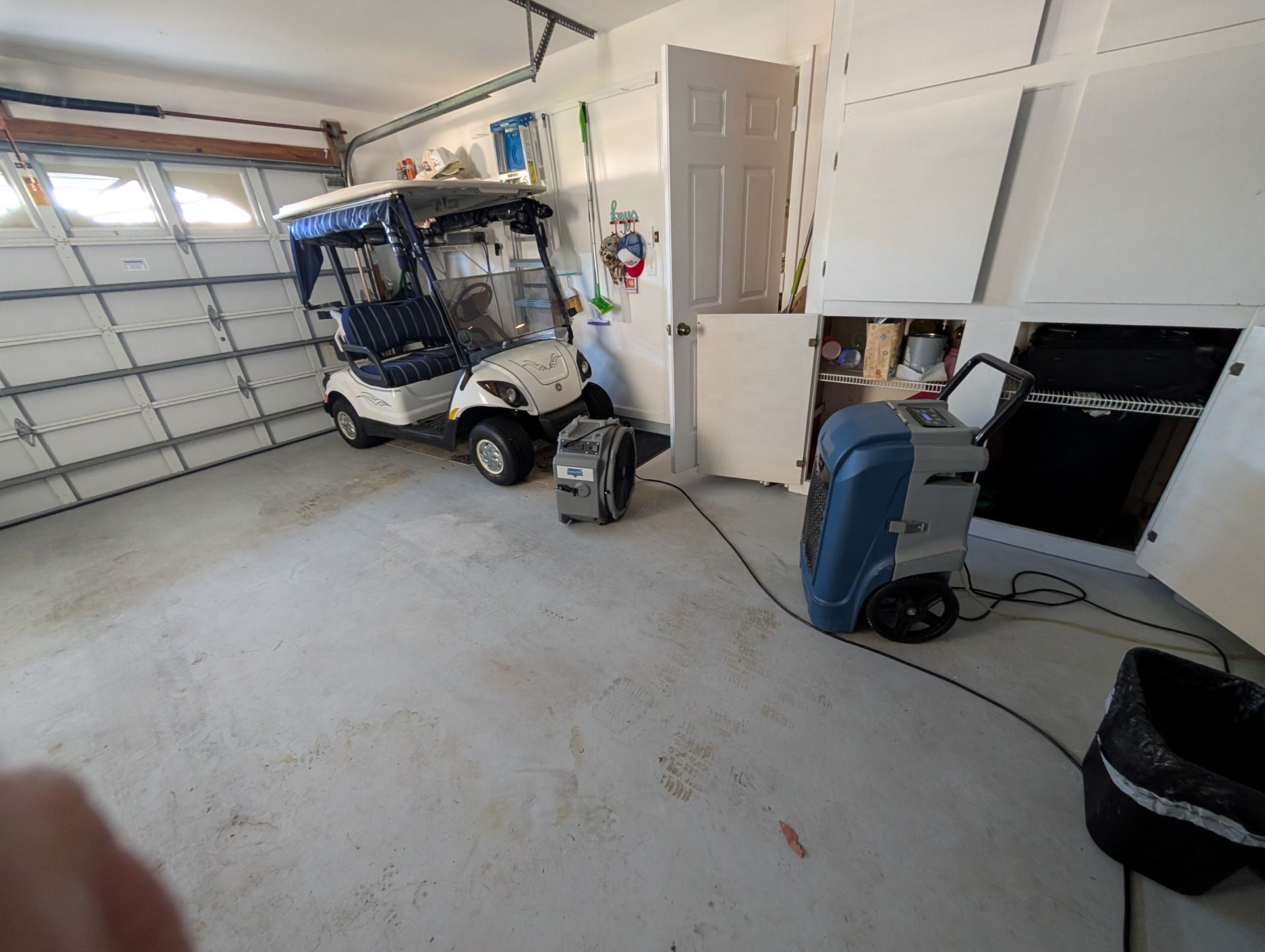 Garage interior with a golf cart, cleaning equipment, and a partially open garage door.