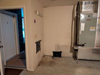 Interior room with door, HVAC unit, vent, and small black space heater on concrete floor.