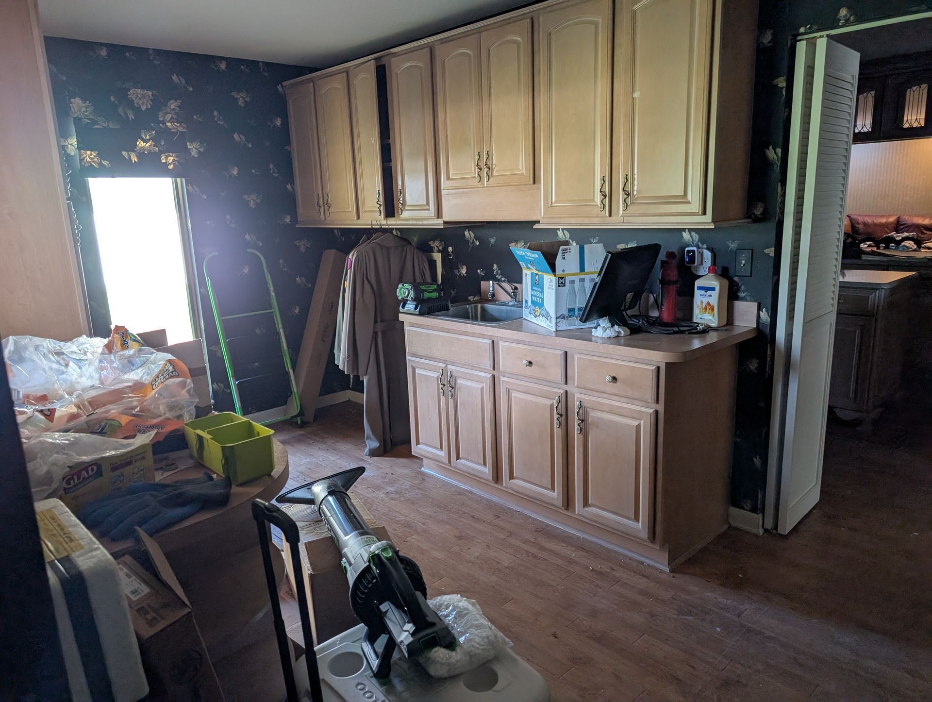 Cluttered kitchen: light cabinets, appliances, and items on the counter, with a window and various objects in the foreground.