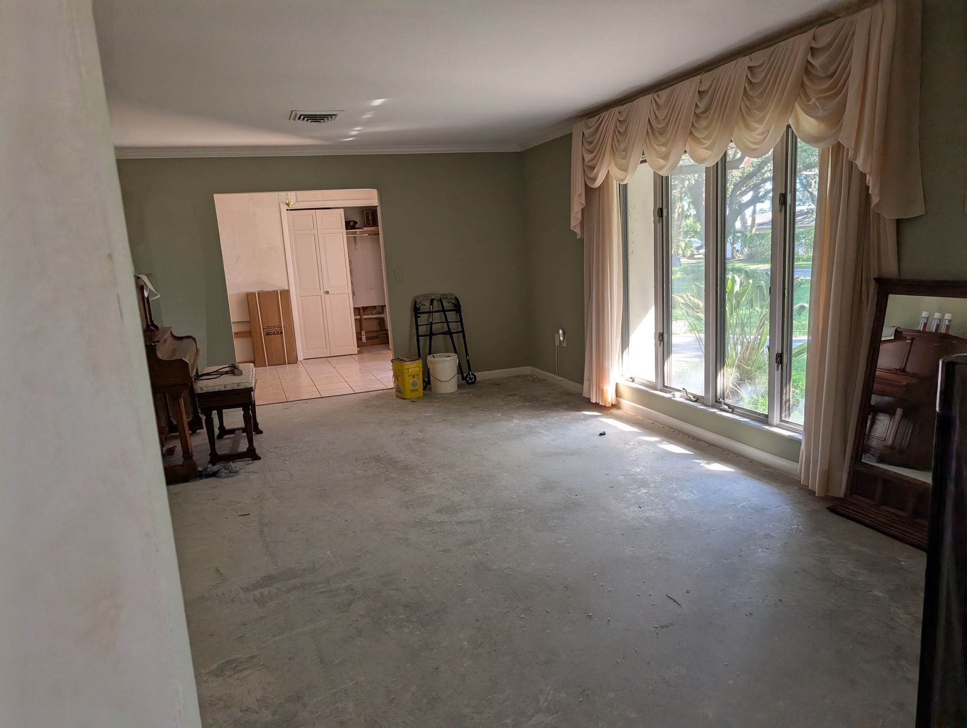 Empty room with large windows, green walls, and concrete floor.