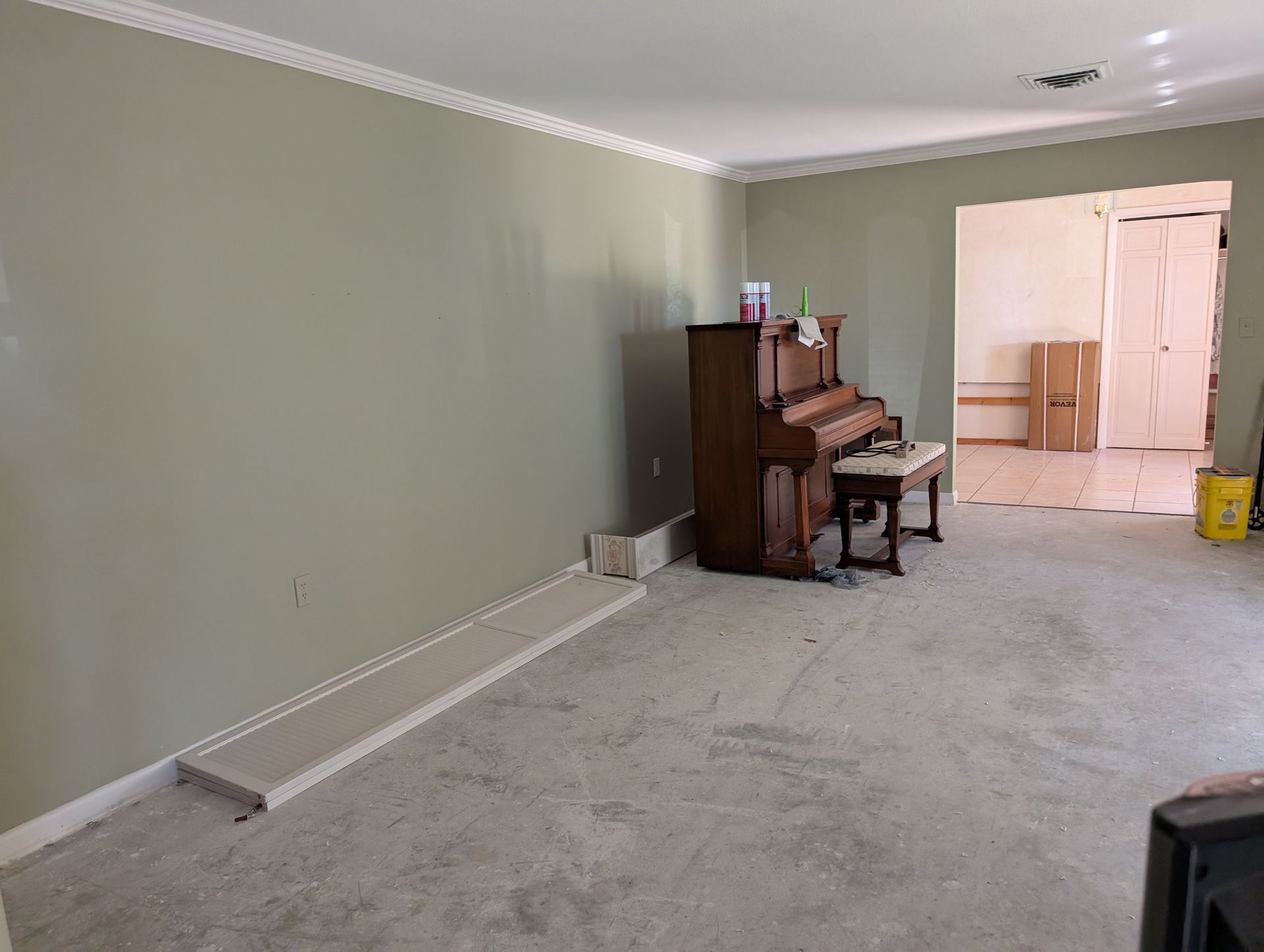 Living room with a piano against a wall; room is being renovated, visible concrete floor.