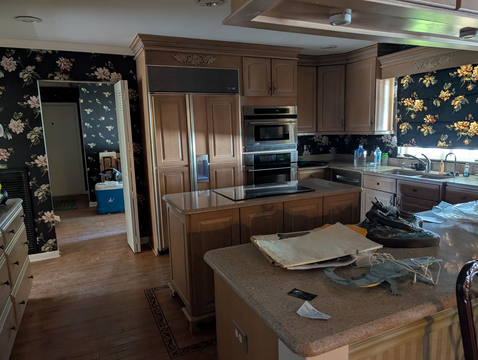 Kitchen with light wood cabinets, granite countertops, and patterned wallpaper. Awaiting cleanup.