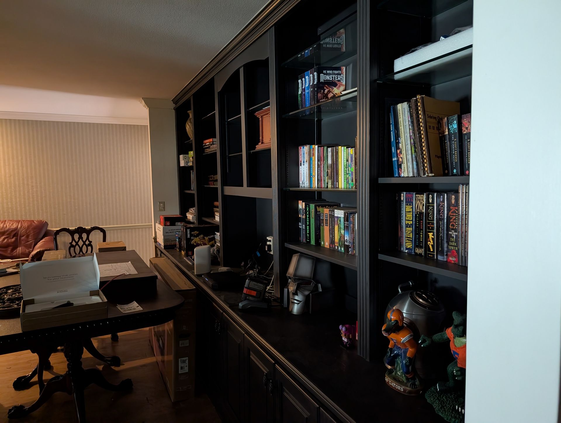 A dark built-in bookcase with books, DVDs, and decorations sits against a wall. A desk with a laptop is in front.