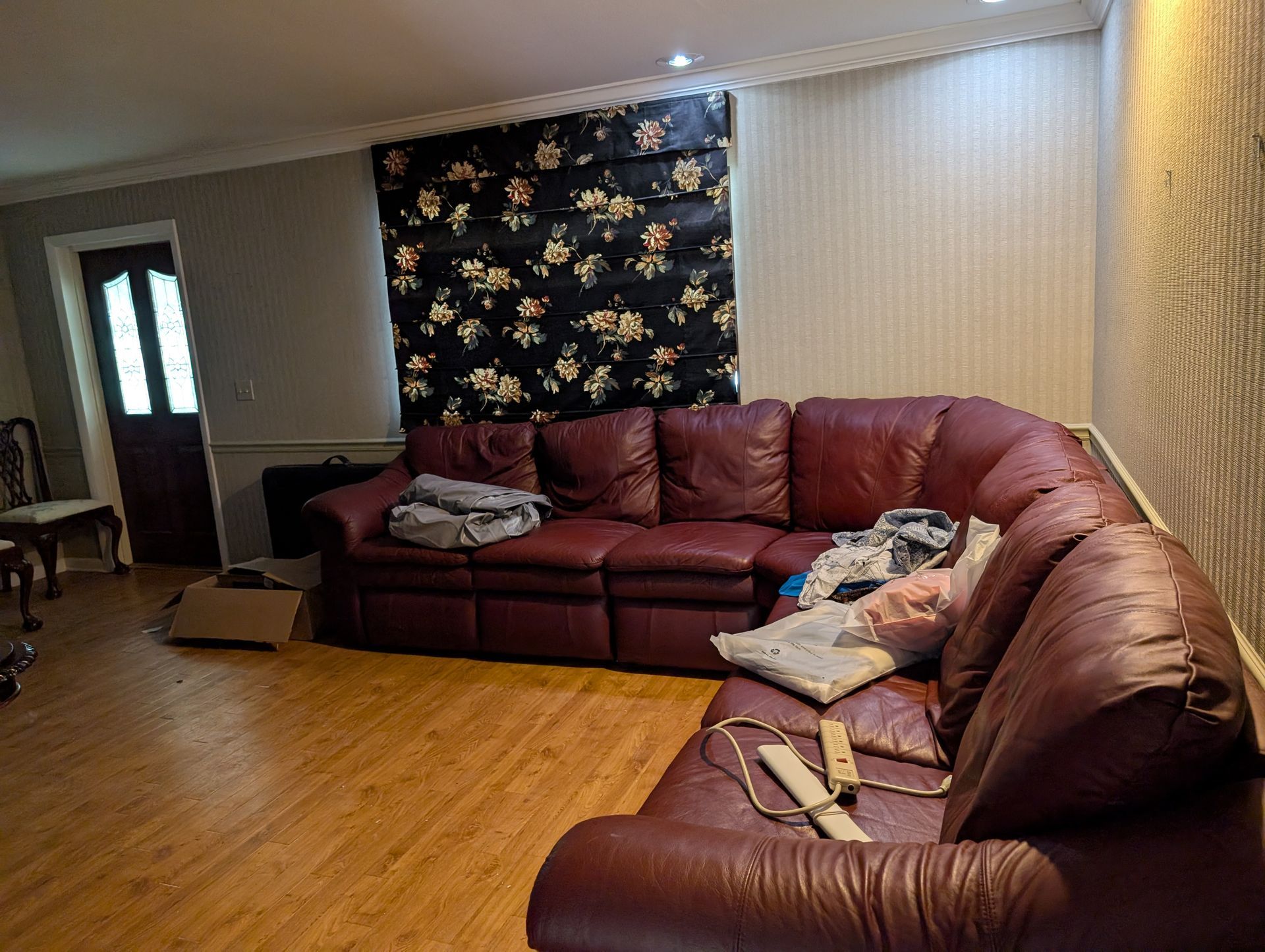 Red leather sectional sofa in a living room, floral patterned curtain, wood floors.