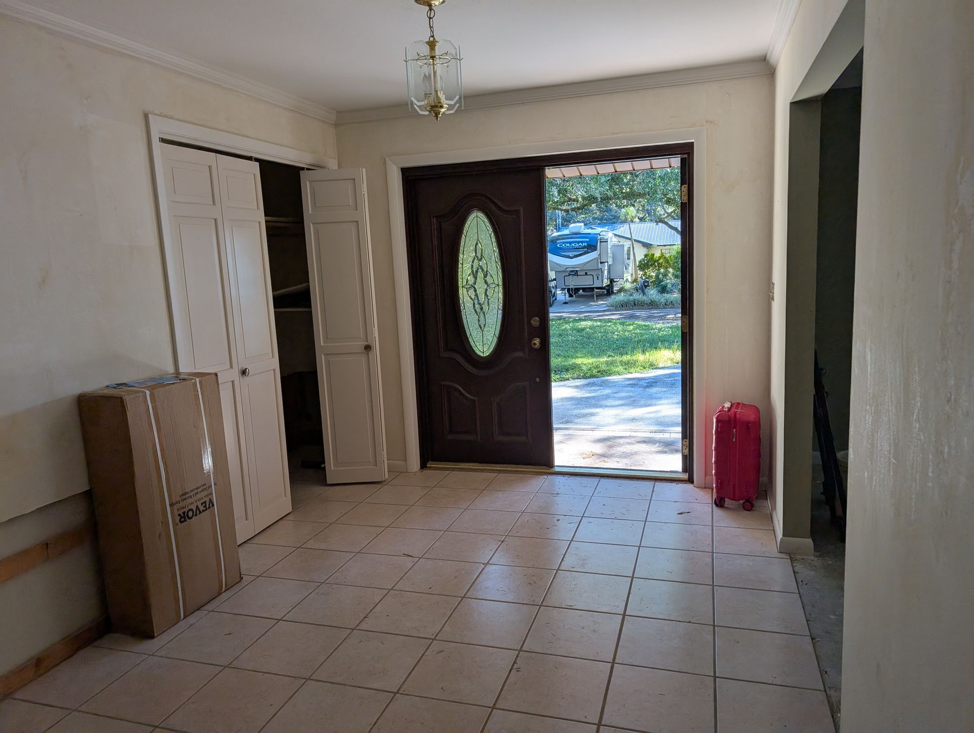 Entryway with tile floor, open door, closet, and a pink suitcase.