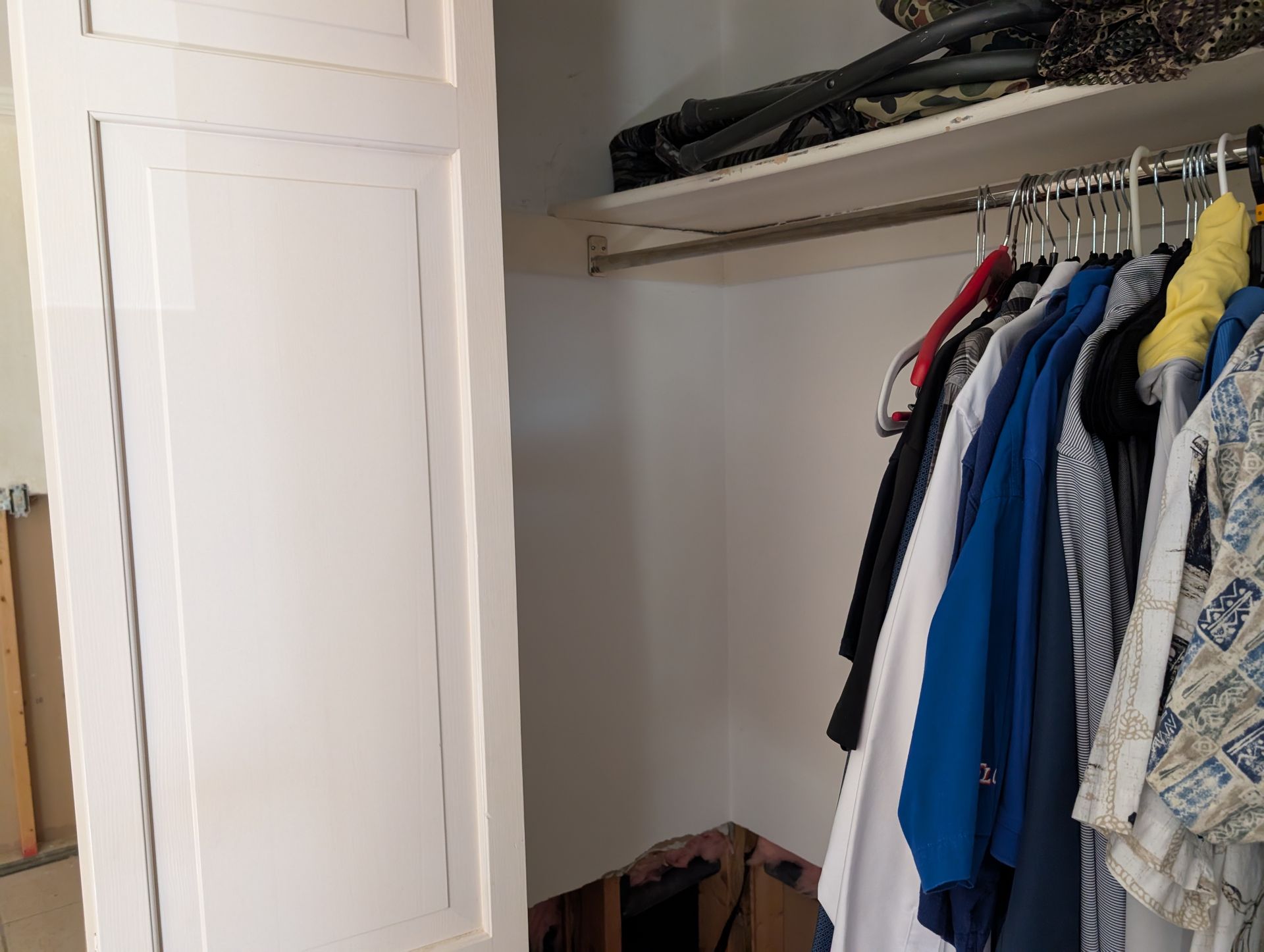 White closet door ajar, clothes hanging on a rod inside, shelf above.