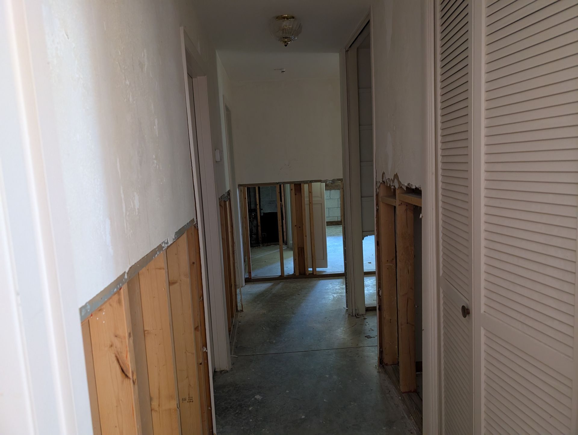 Hallway with exposed wood studs, damaged walls, and a closed door on the right.