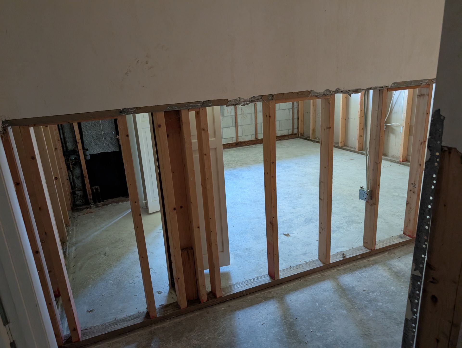 Interior view of a room under construction, showing wooden studs framing the walls and opening to the room.