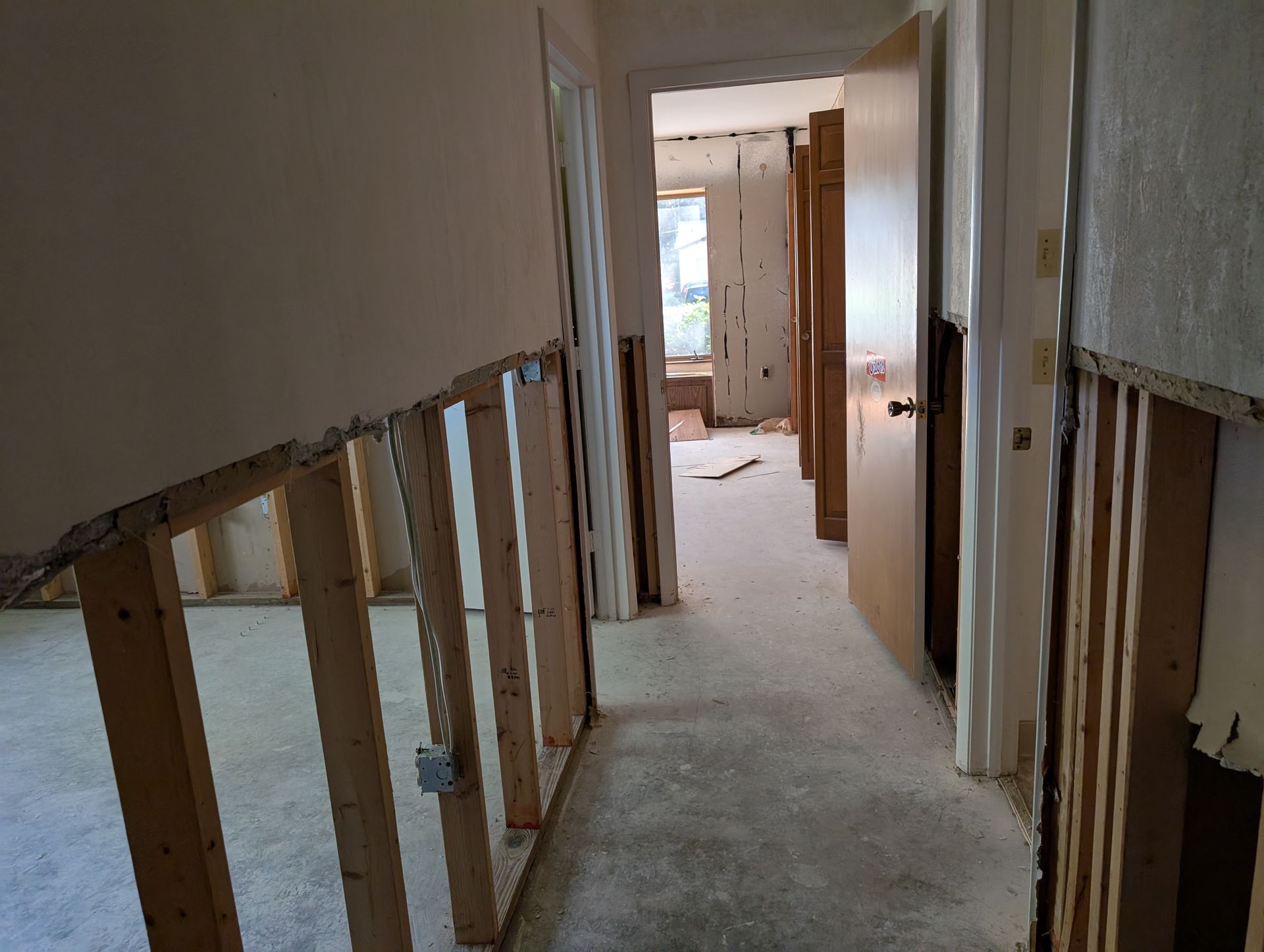 Hallway under renovation with exposed wall studs and debris on the floor.