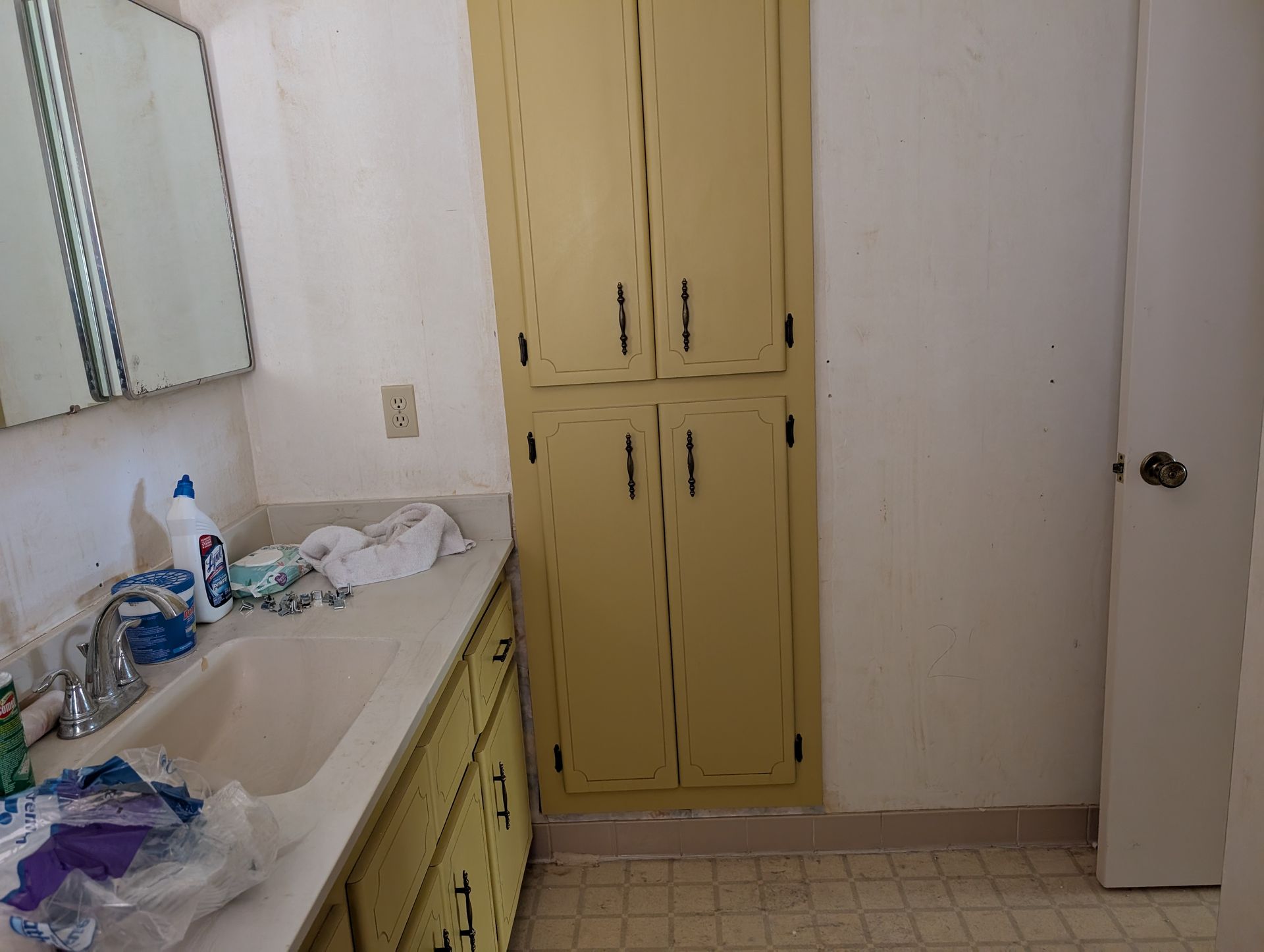 Bathroom with sink, mirror, yellow cabinets, white walls, and a closed door.