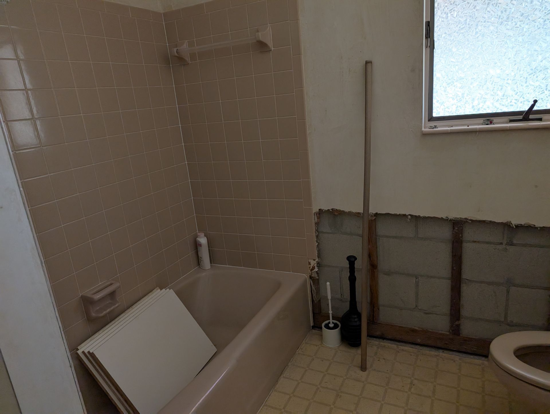 Bathroom with a bathtub, partially tiled walls, and exposed studs near the toilet.