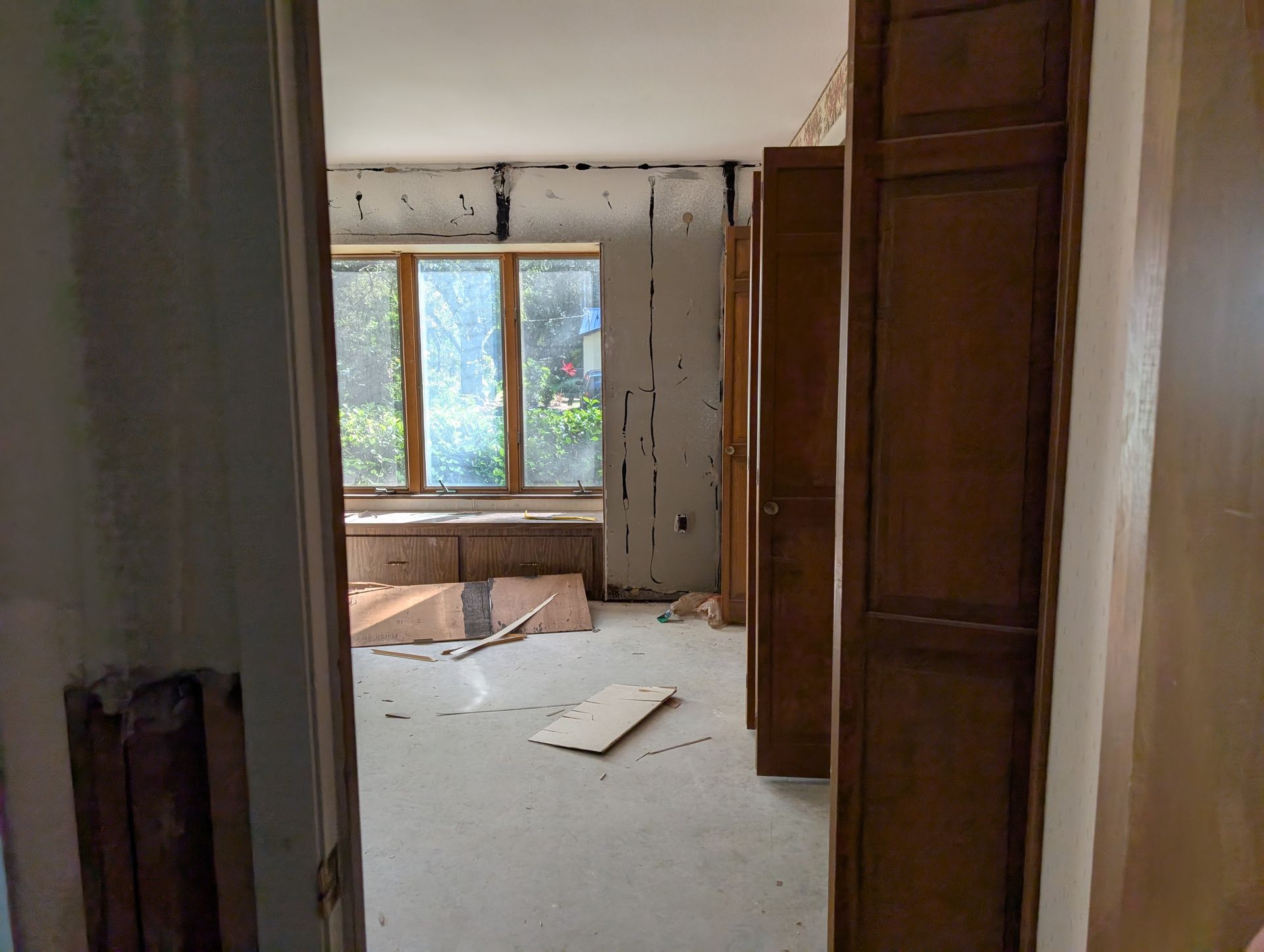 Interior room undergoing renovation with wooden cabinets, window, and debris.