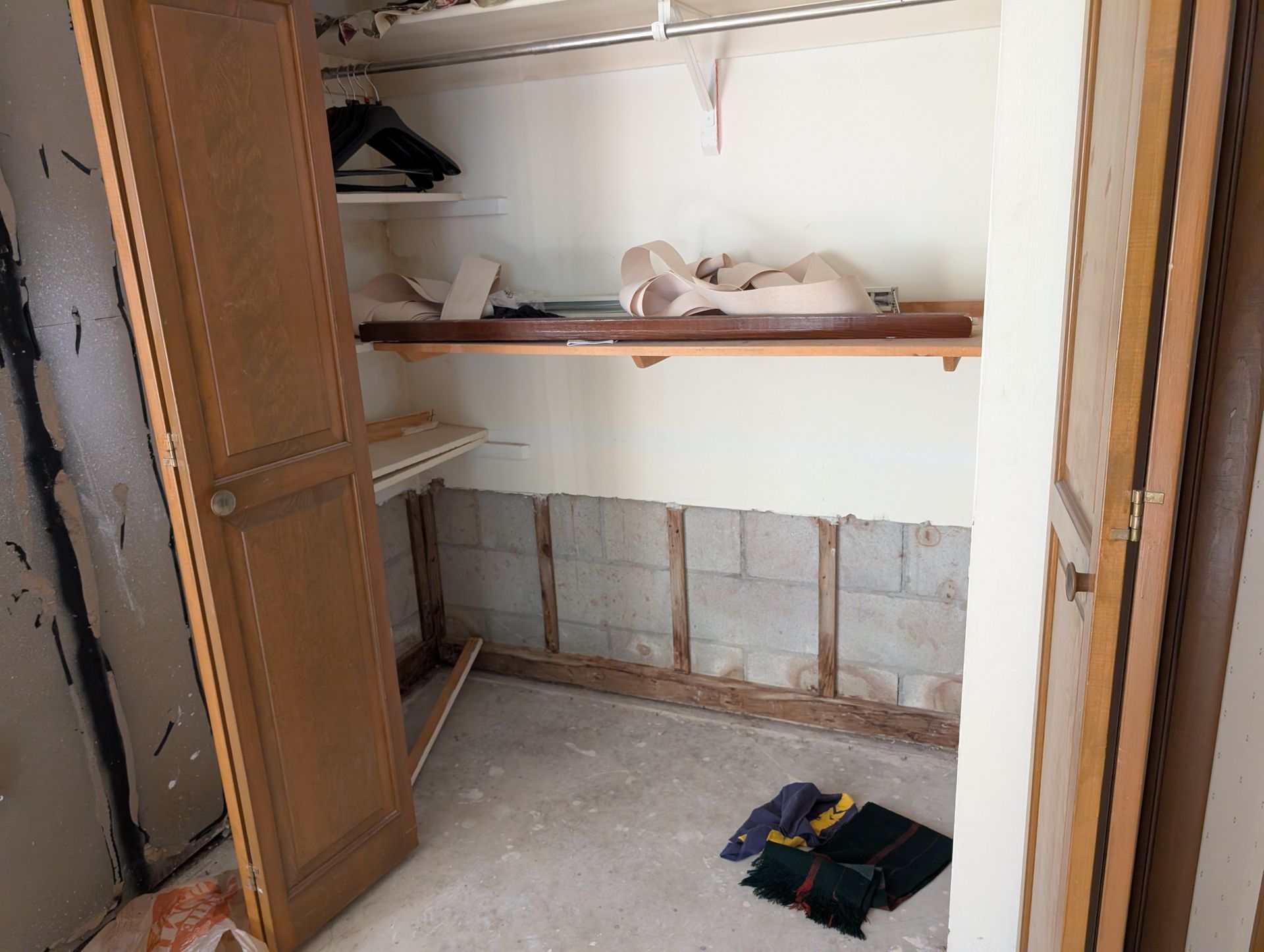 Empty closet with partial wall demolition, wooden shelves, and open door.