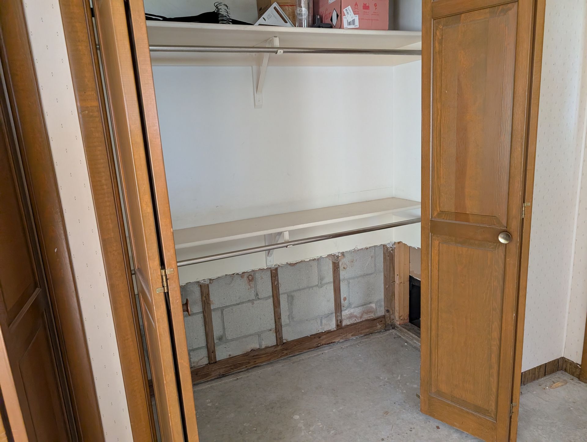 Closet interior with wooden doors, a shelf, and cinder block foundation visible below.