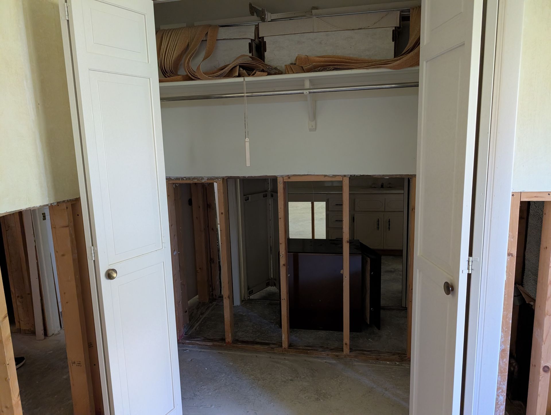 Open closet with visible studs, doorway to another room, exposed ceiling.