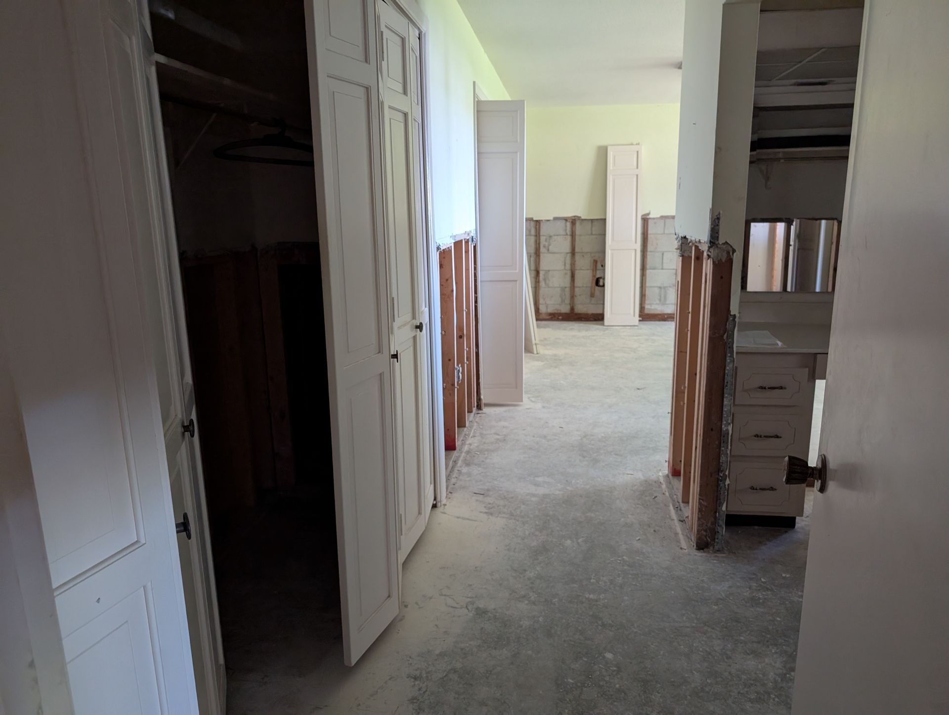 Interior of a room under renovation. Closet door open, bare floors and cabinets, walls partially finished.