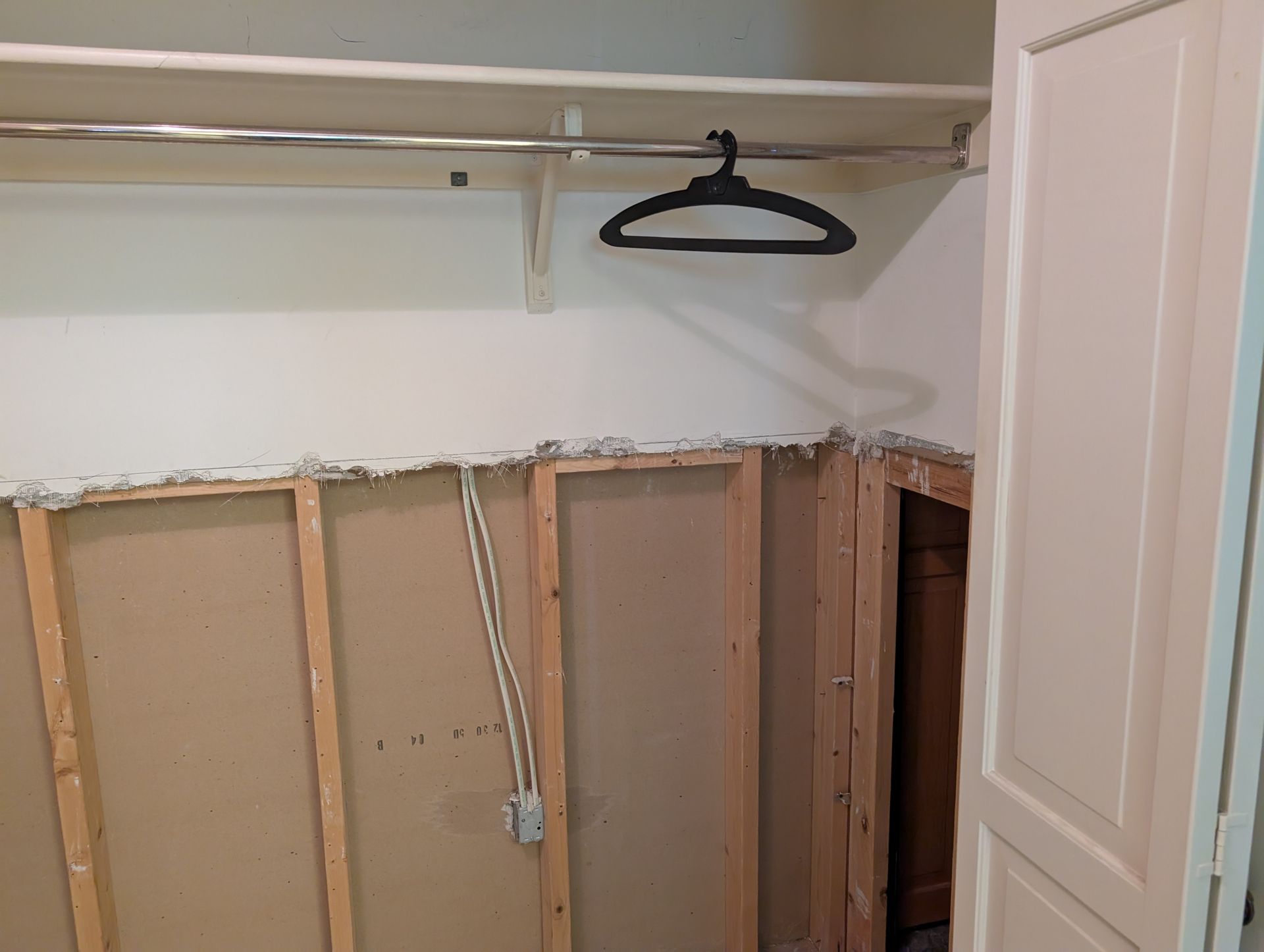 Closet interior with exposed wall studs, hanging rod, shelf, and a hanger.