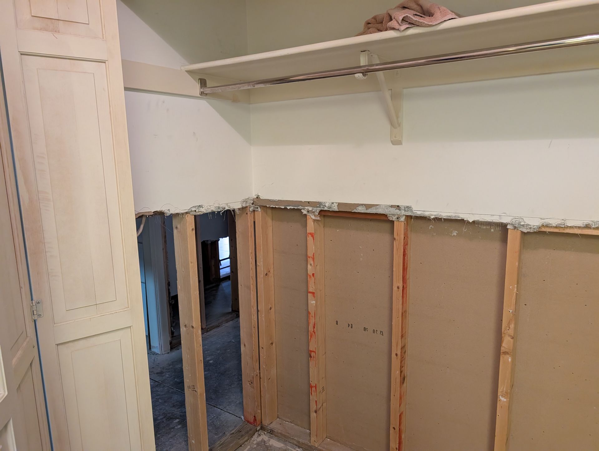 Interior view of a room under renovation. Exposed wall studs, partial drywall, and a shelf are visible.