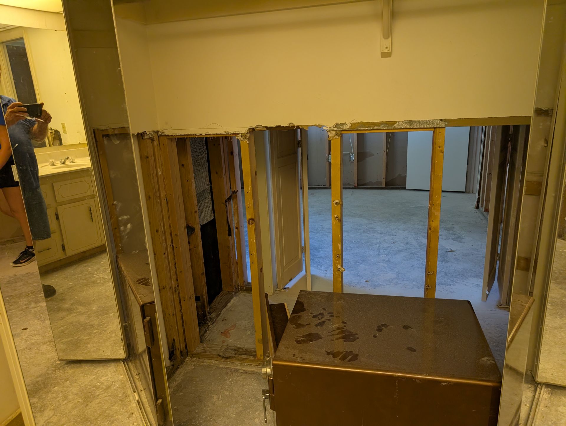 Room under construction. Wall removed exposing studs, drywall debris on floor. Cabinet in foreground.