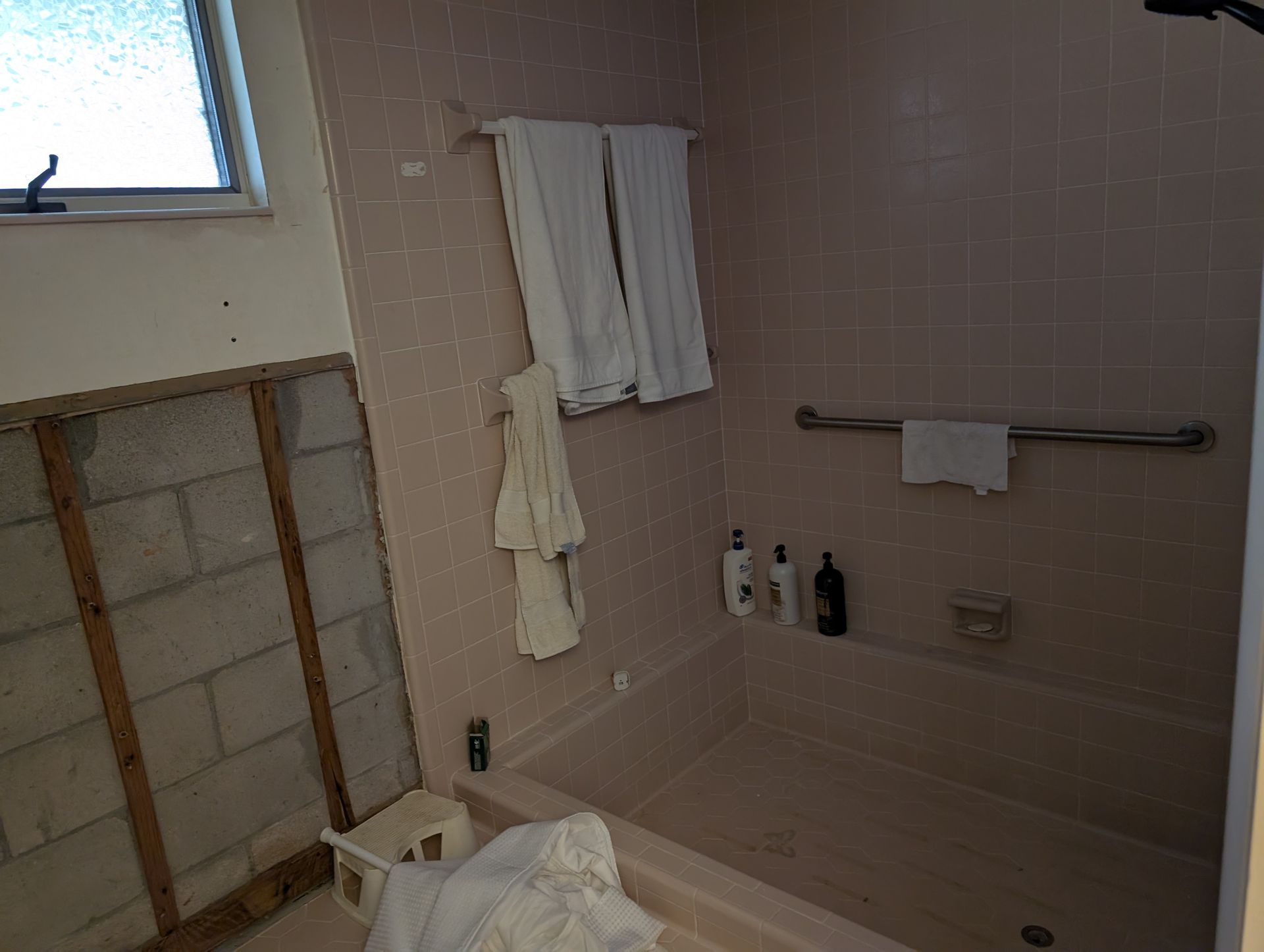 Bathroom with pink tile, a tub, towels, a grab bar, and exposed wall studs.