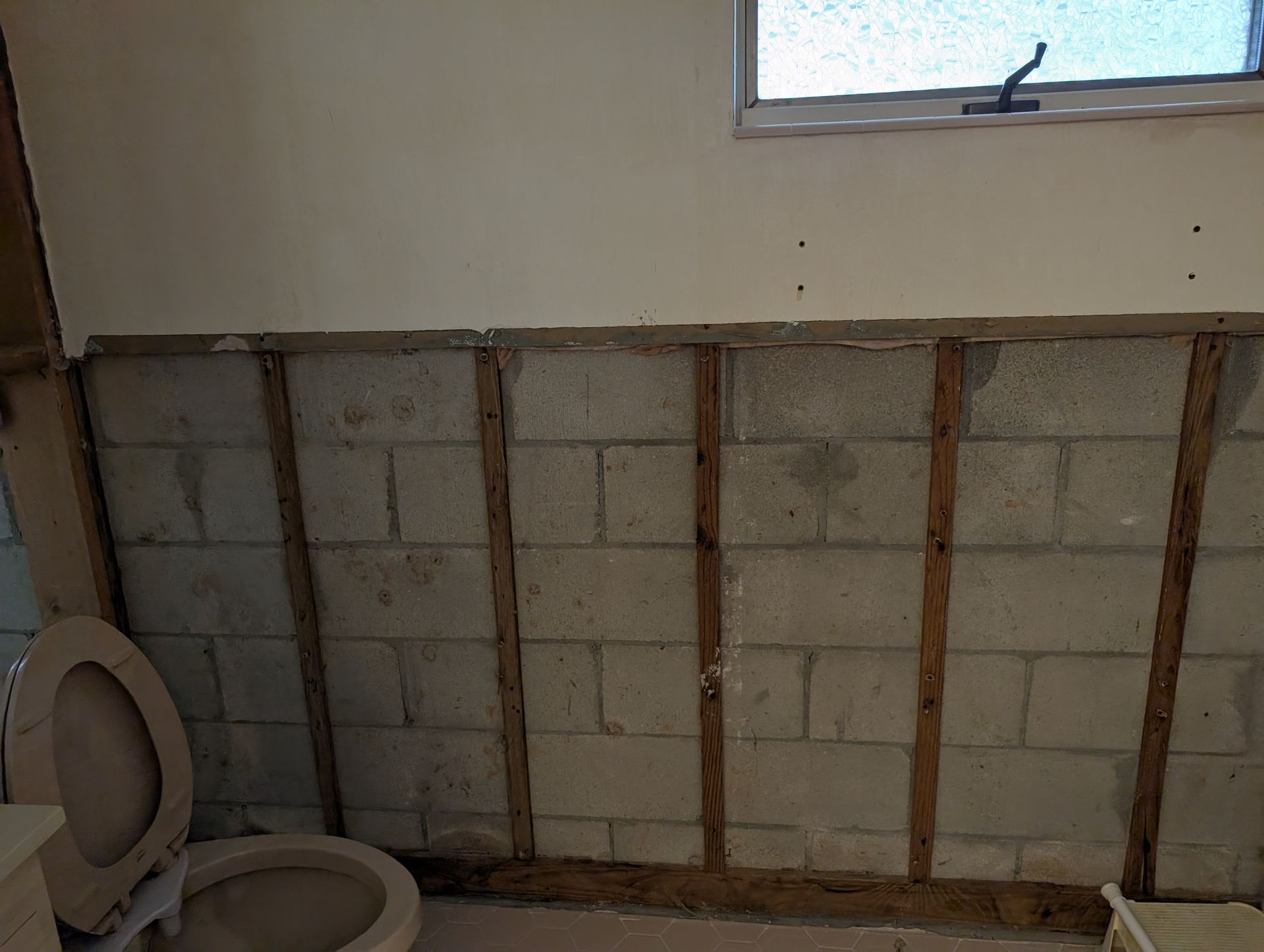 Bathroom interior with exposed cinder block wall, wooden beams, toilet, and window.