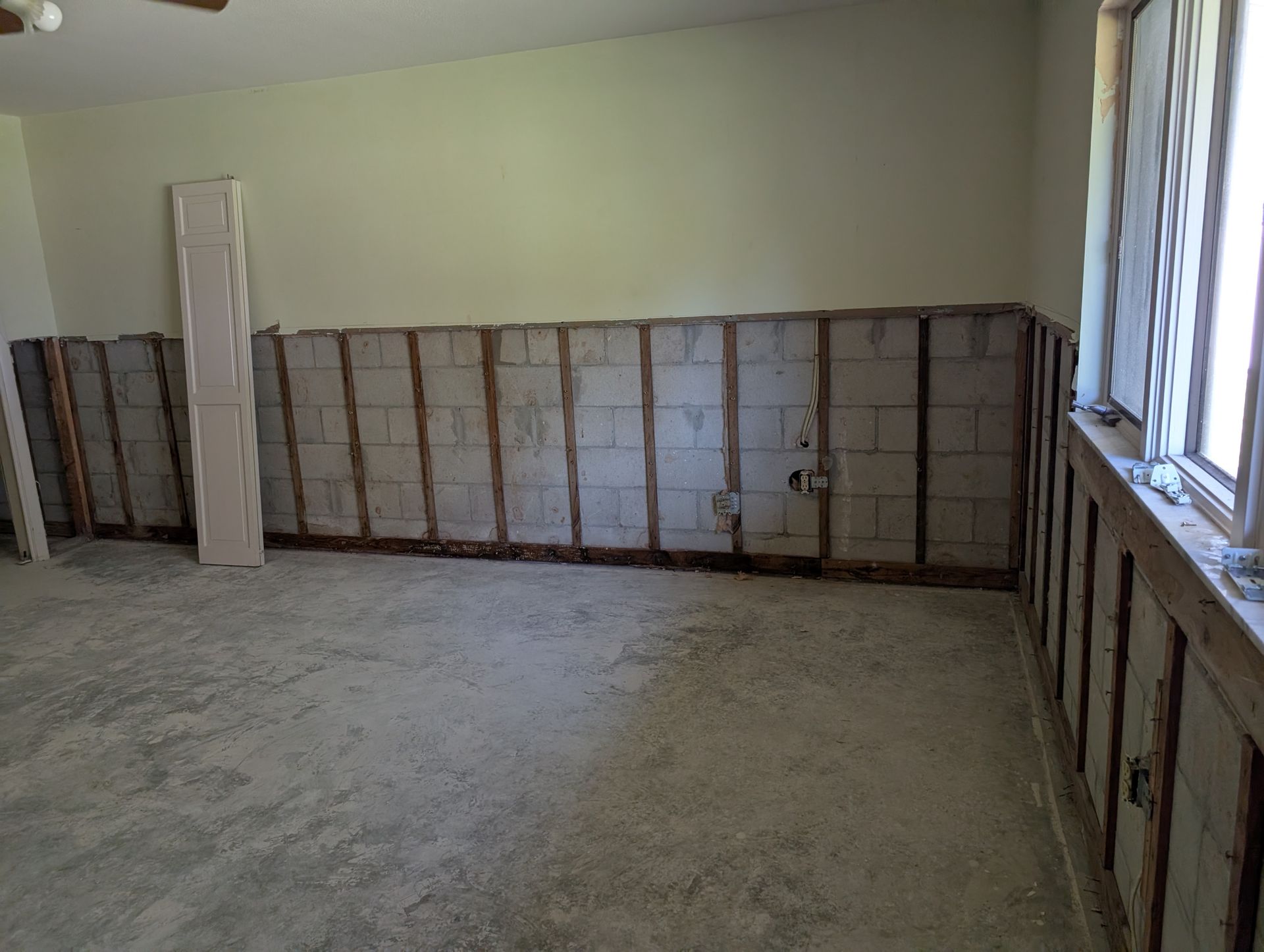 Interior room with exposed cinder block wall. Drywall and insulation removed. Window on right.