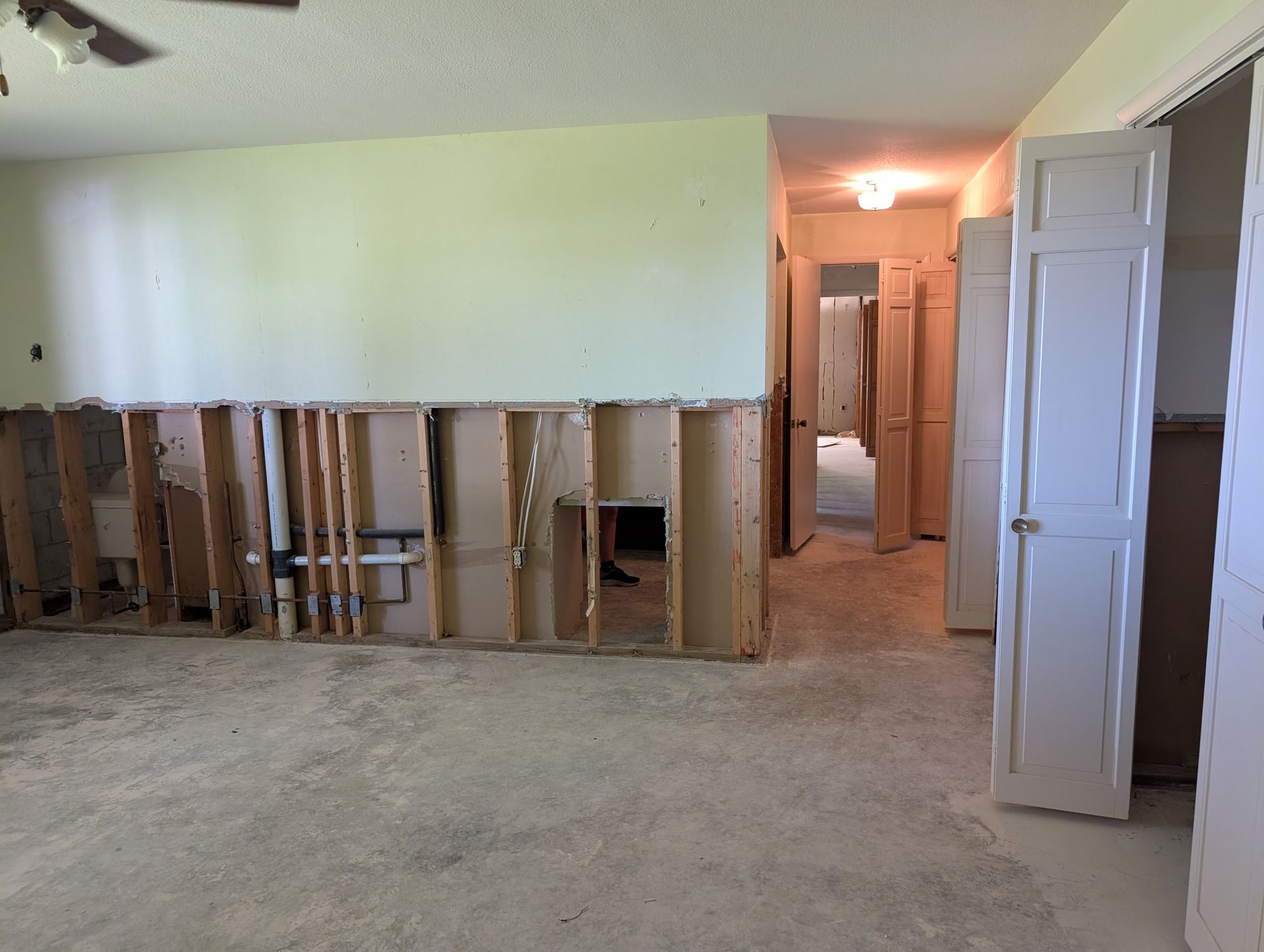 Interior view of a room with exposed wall studs, removed drywall, and a hallway.