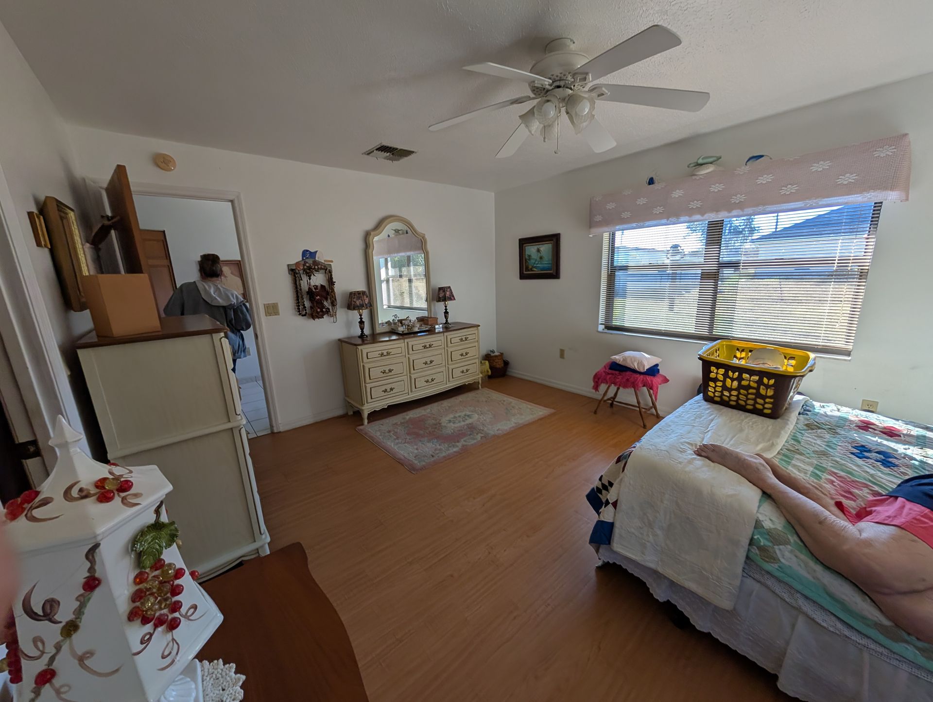 Bedroom with a bed, dresser, window, ceiling fan, and person resting on the bed.