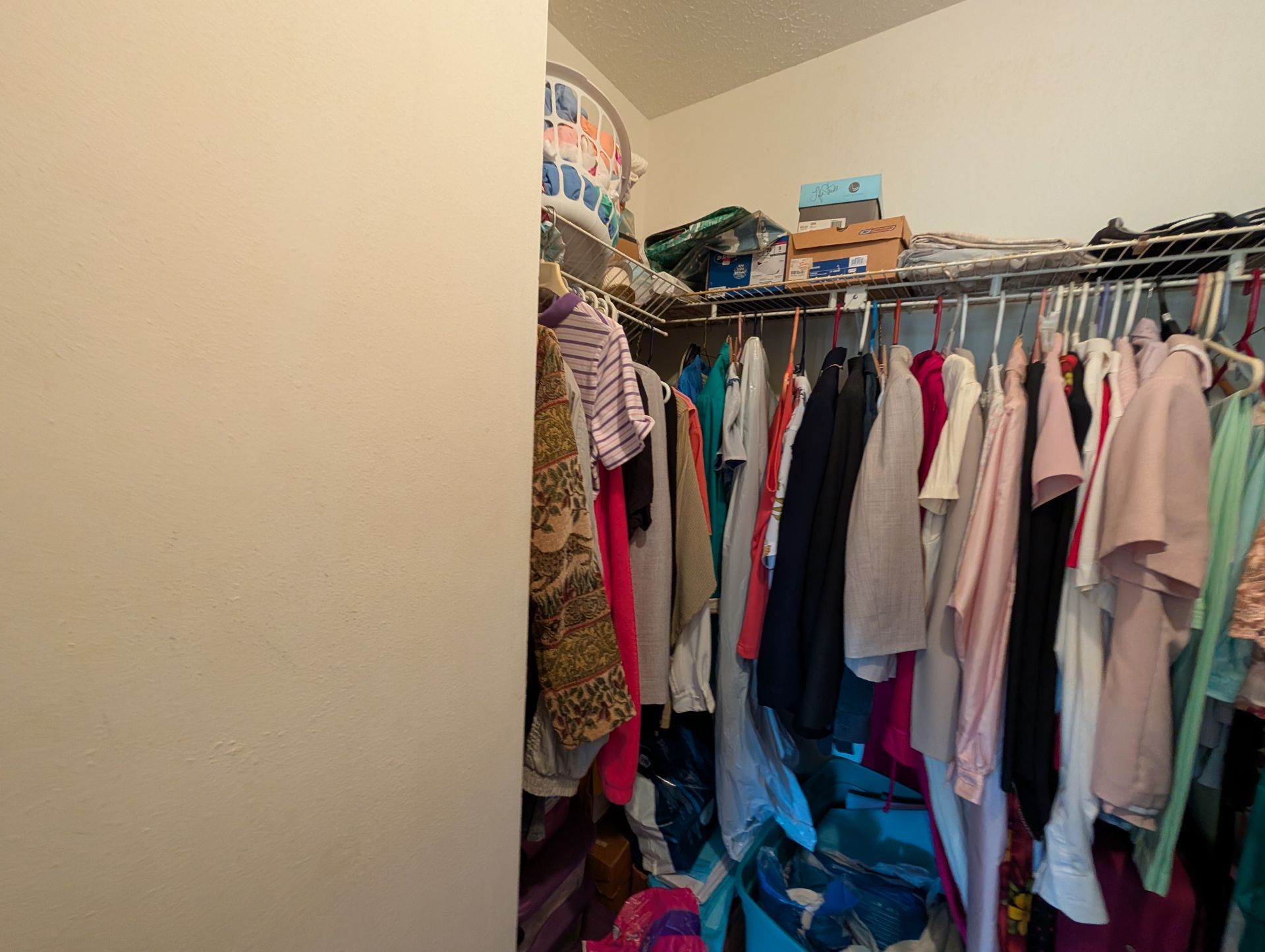 Walk-in closet with clothes hanging on racks, cluttered with items on shelves.