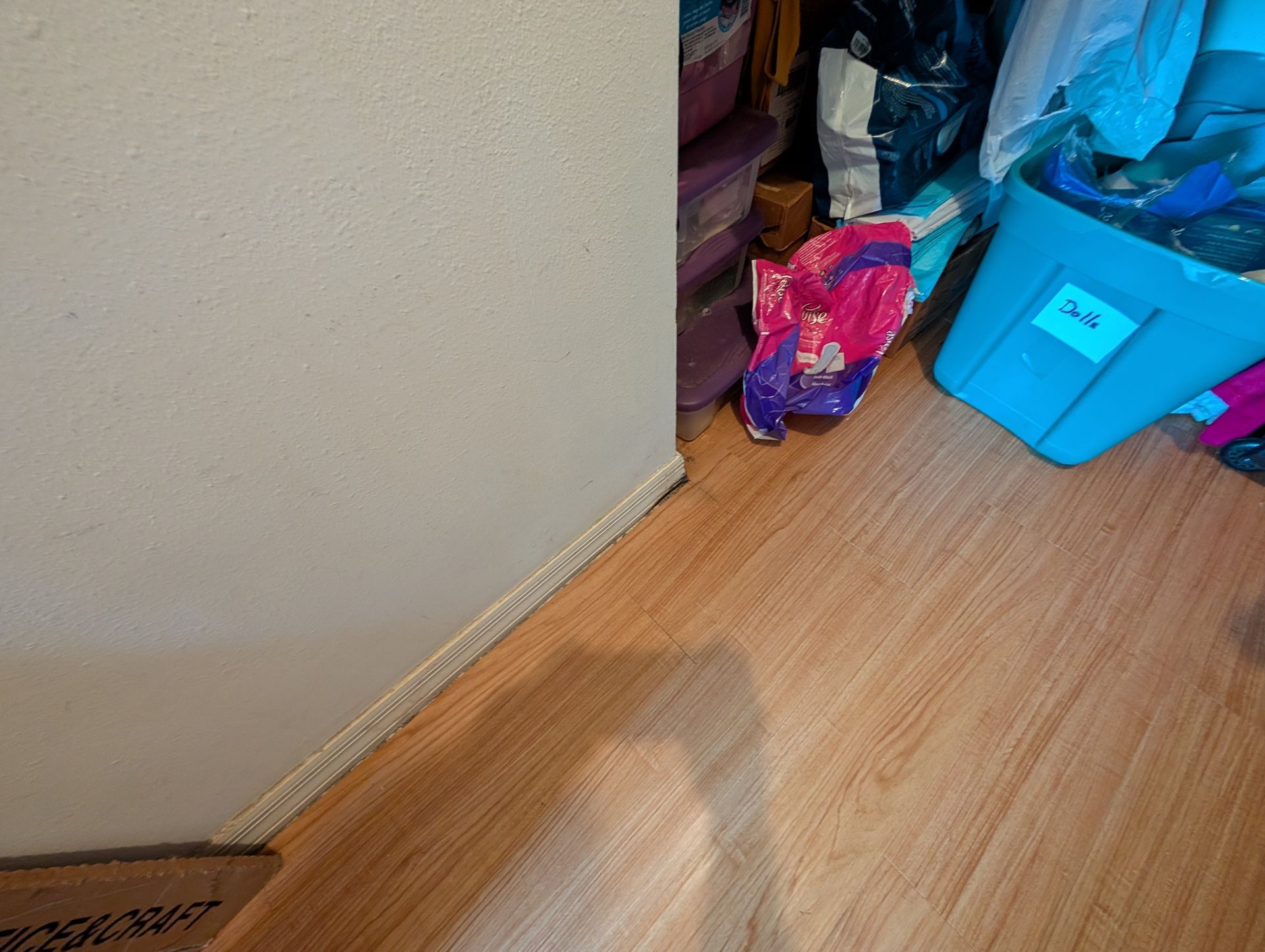 Corner of room with tan wall, wooden floor, and storage bins.