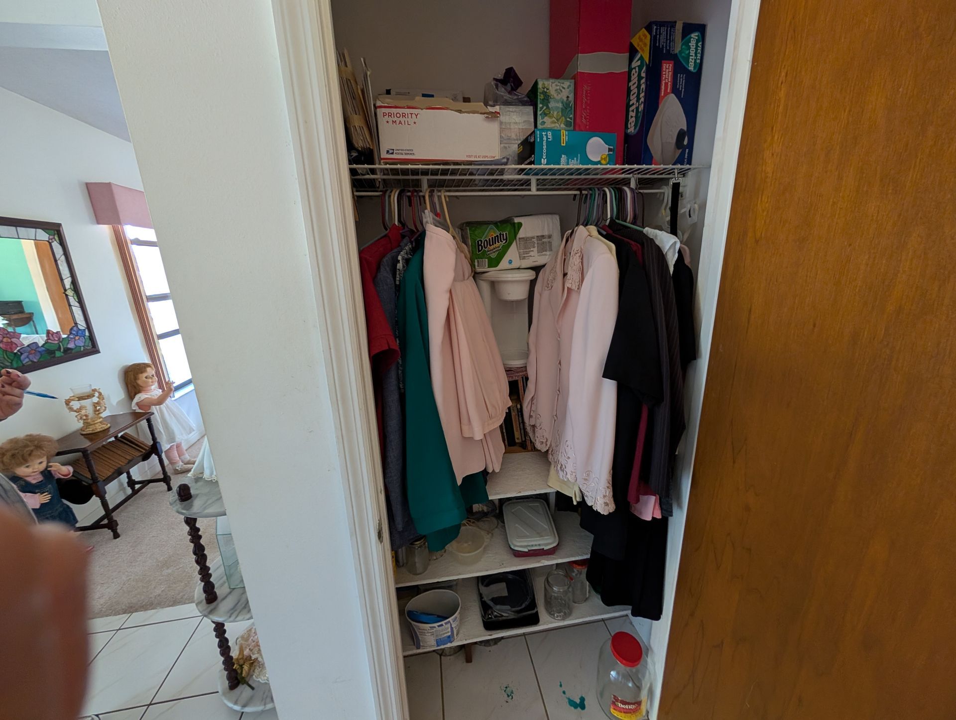 Closet with clothes on hangers and items on shelves; a person's hand partially visible on the left.