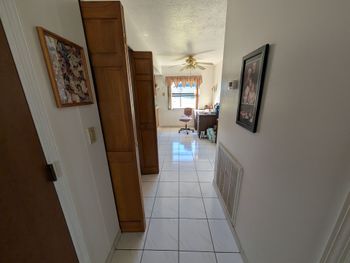 Hallway with tile floor, bookshelves, and doorway leading to a room with desk and chair.
